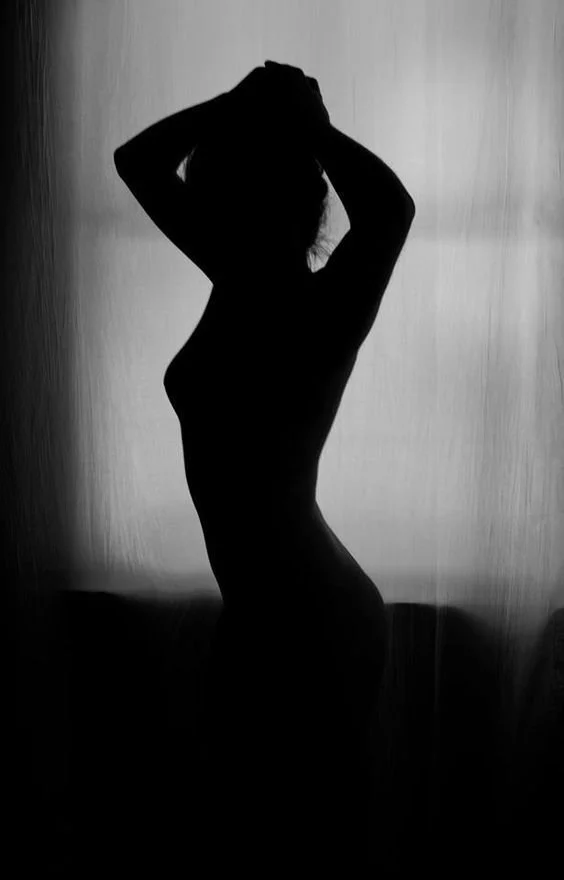 Silhouette of a woman standing with her hands in her hair, backlit against a plain background.