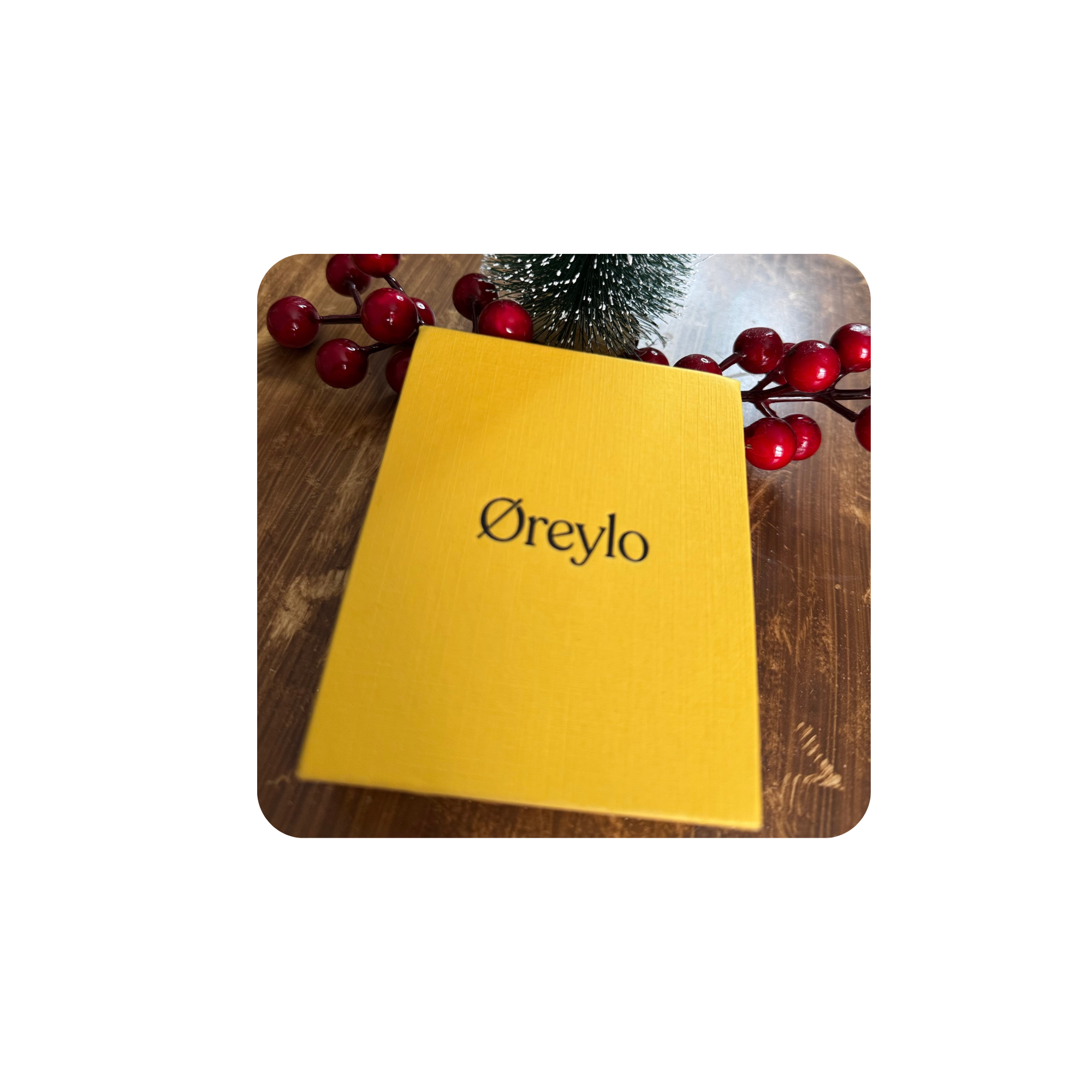 Yellow box with 'Øreyo' text, surrounded by red berries and a small green Christmas tree on a wooden surface.