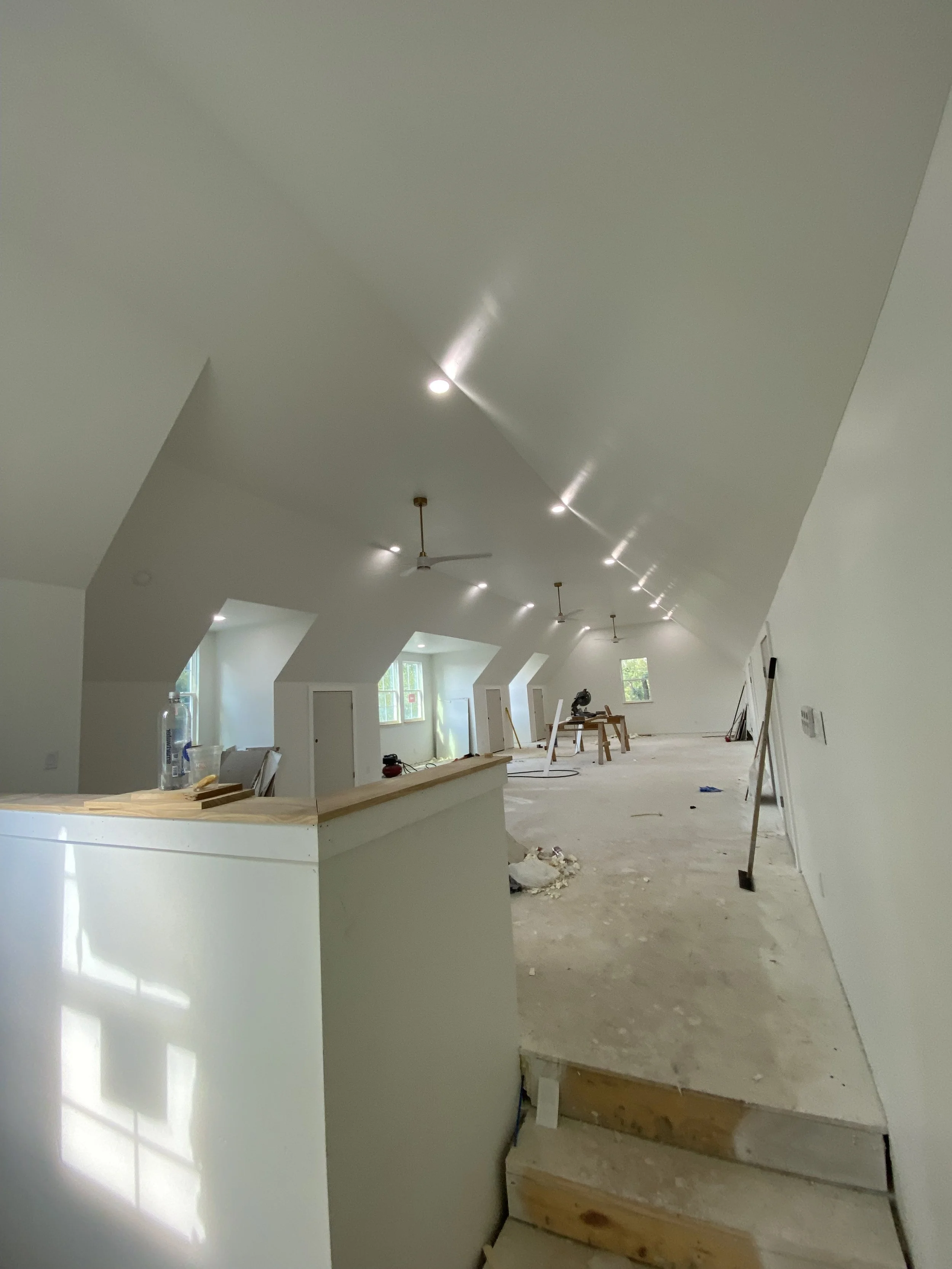 Interior of a room under construction with a sloped ceiling, multiple windows, and tools and materials scattered around.