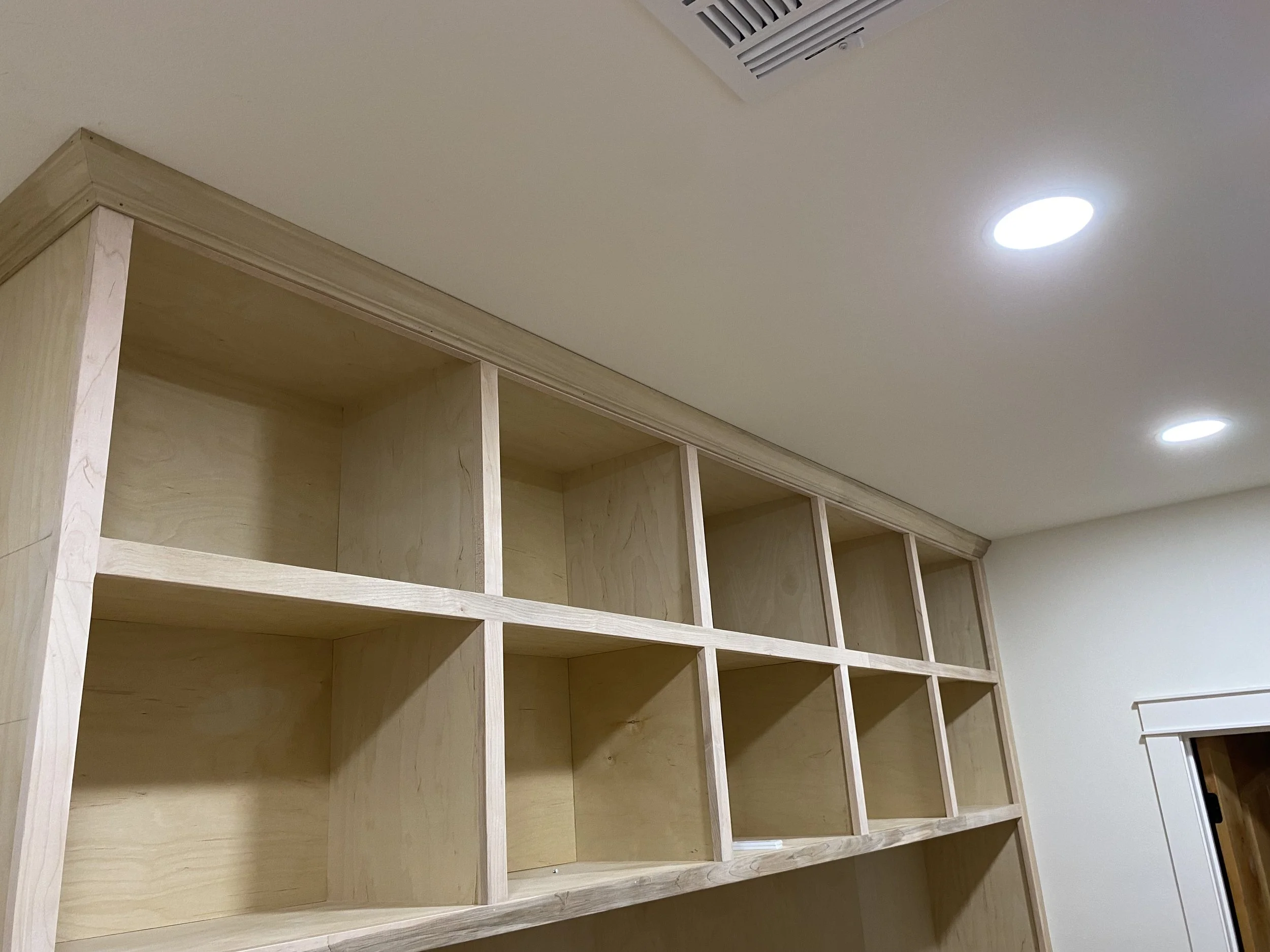 unfinished wooden built-in shelving unit in a room with recessed ceiling lights.