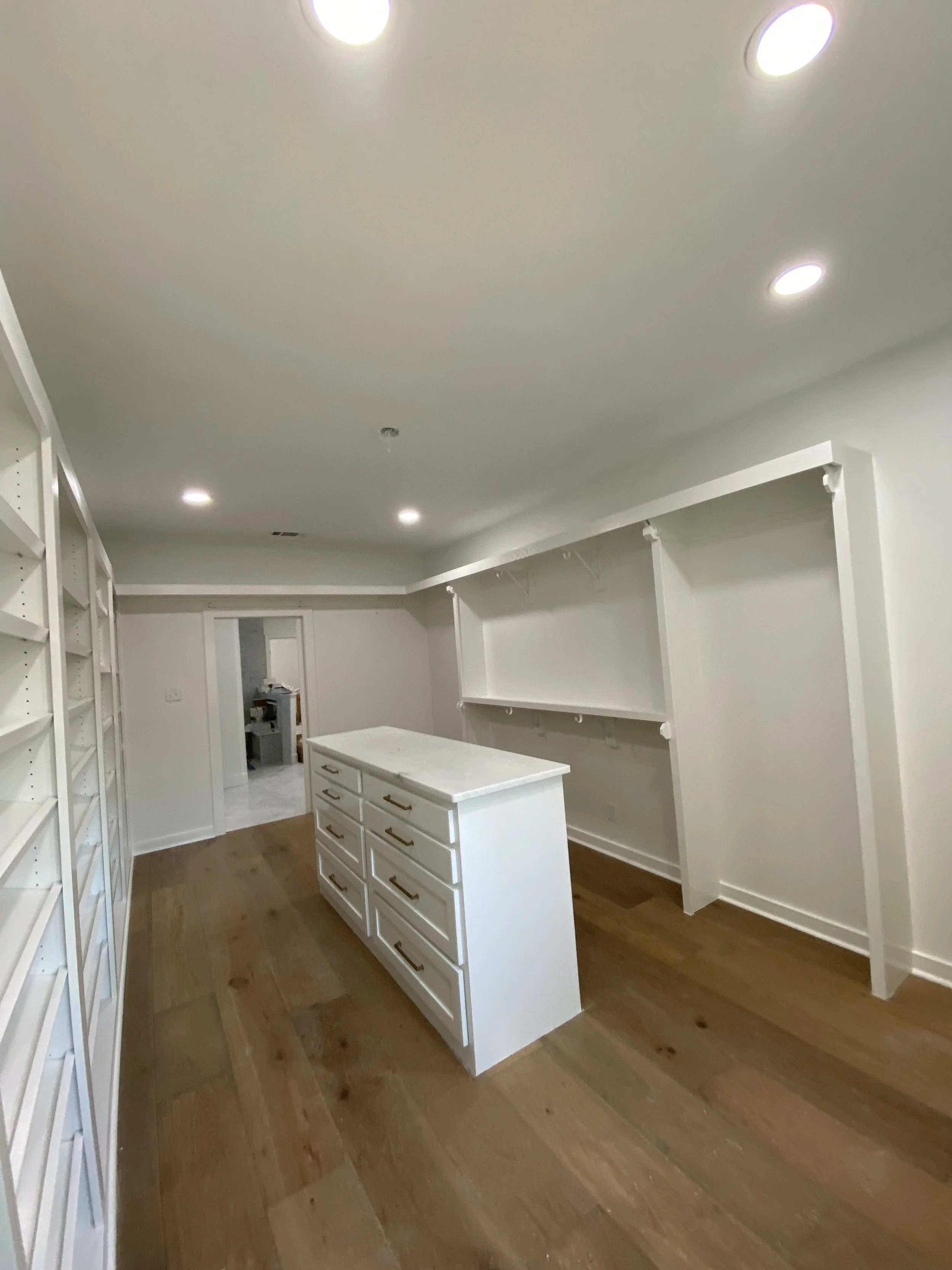 Empty walk-in closet with white built-in shelves and drawers, a central island with drawers, and a wooden floor.