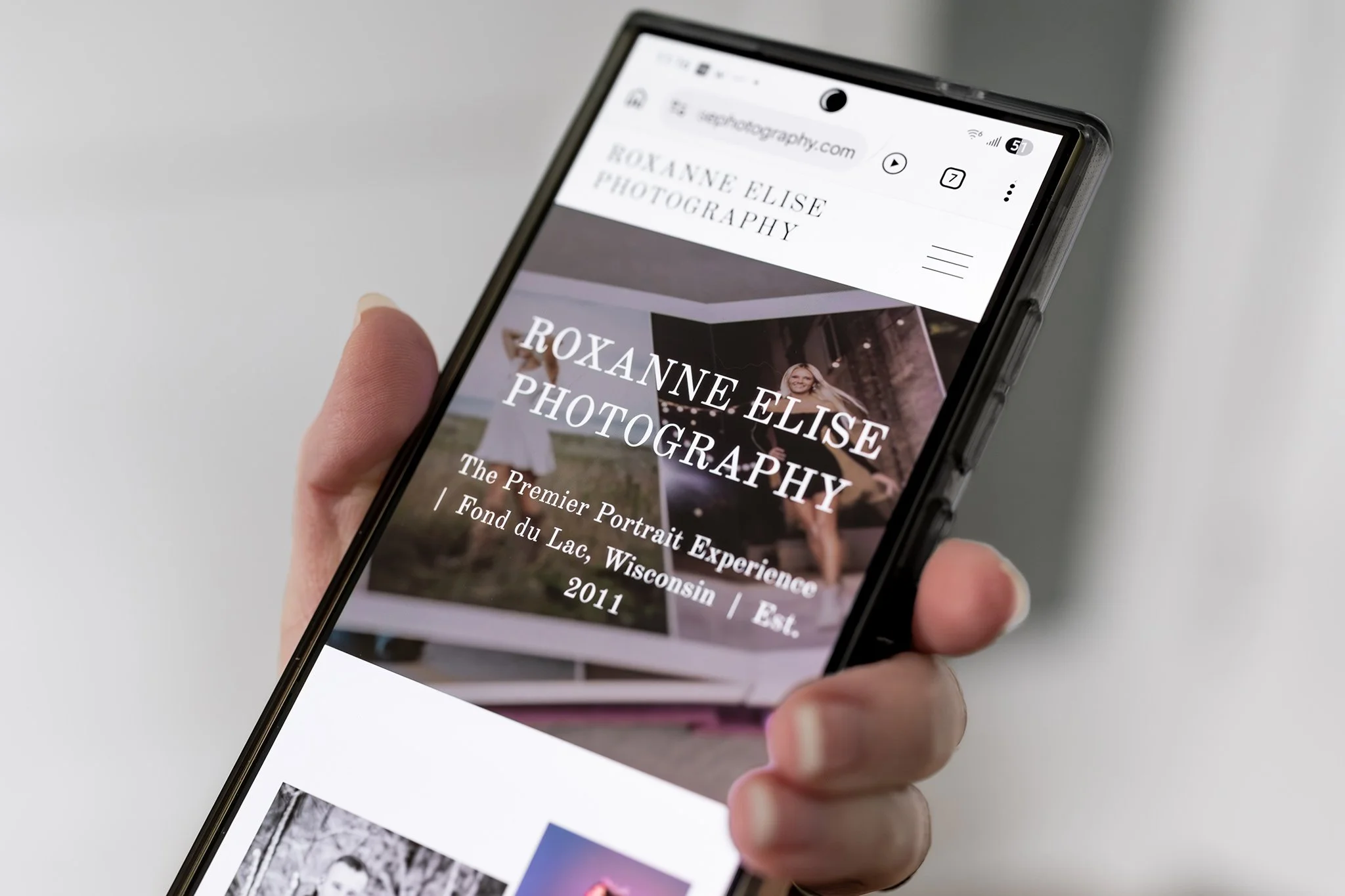 Close-up of a mobile phone screen held in a hand, displaying the home page of Roxanne Elise Photography's website