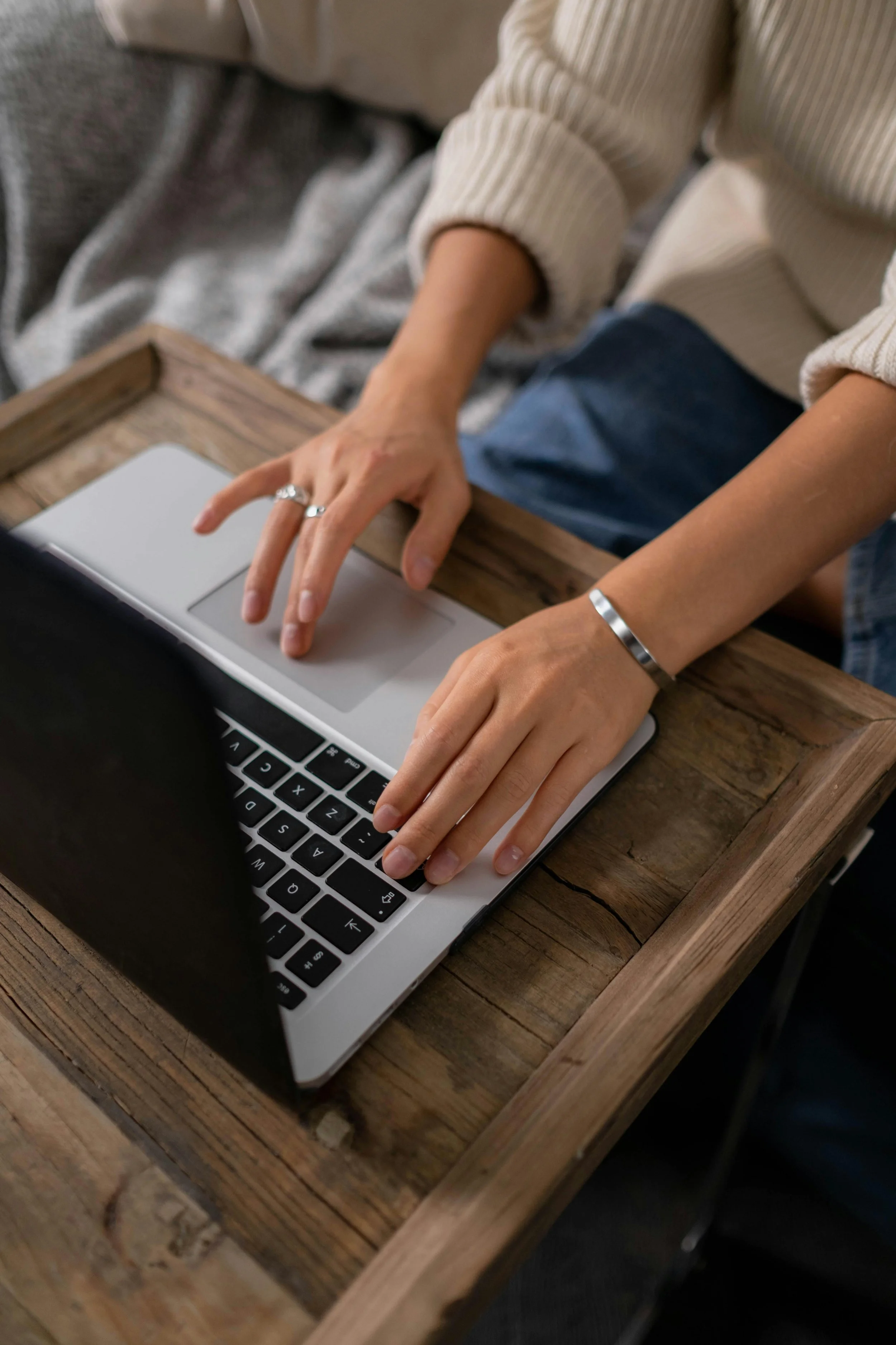 Top view of female hands typing on a Macbook laptop, with the laptop sitting on a wooden surface.