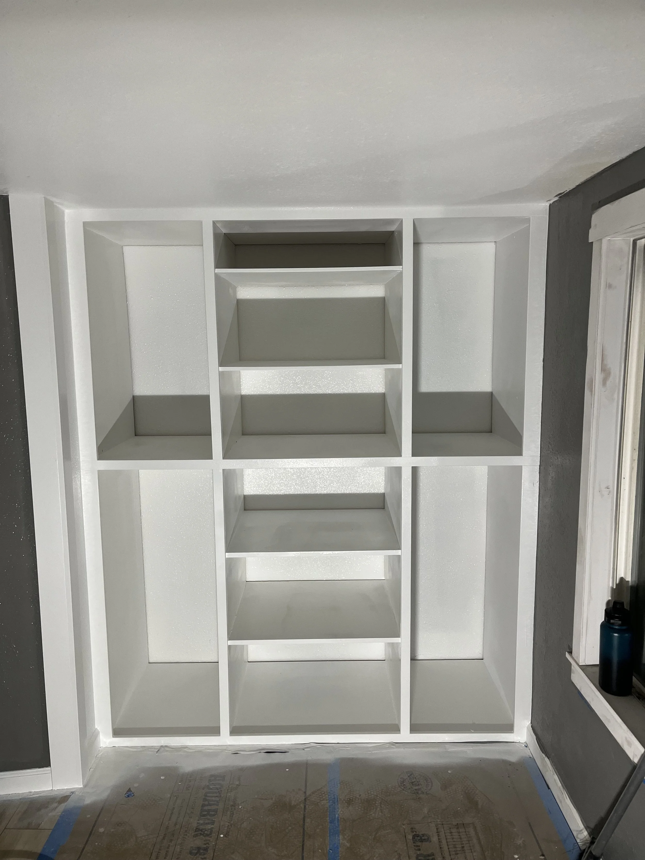 Built-in white shelving unit with various compartments in a room under construction.