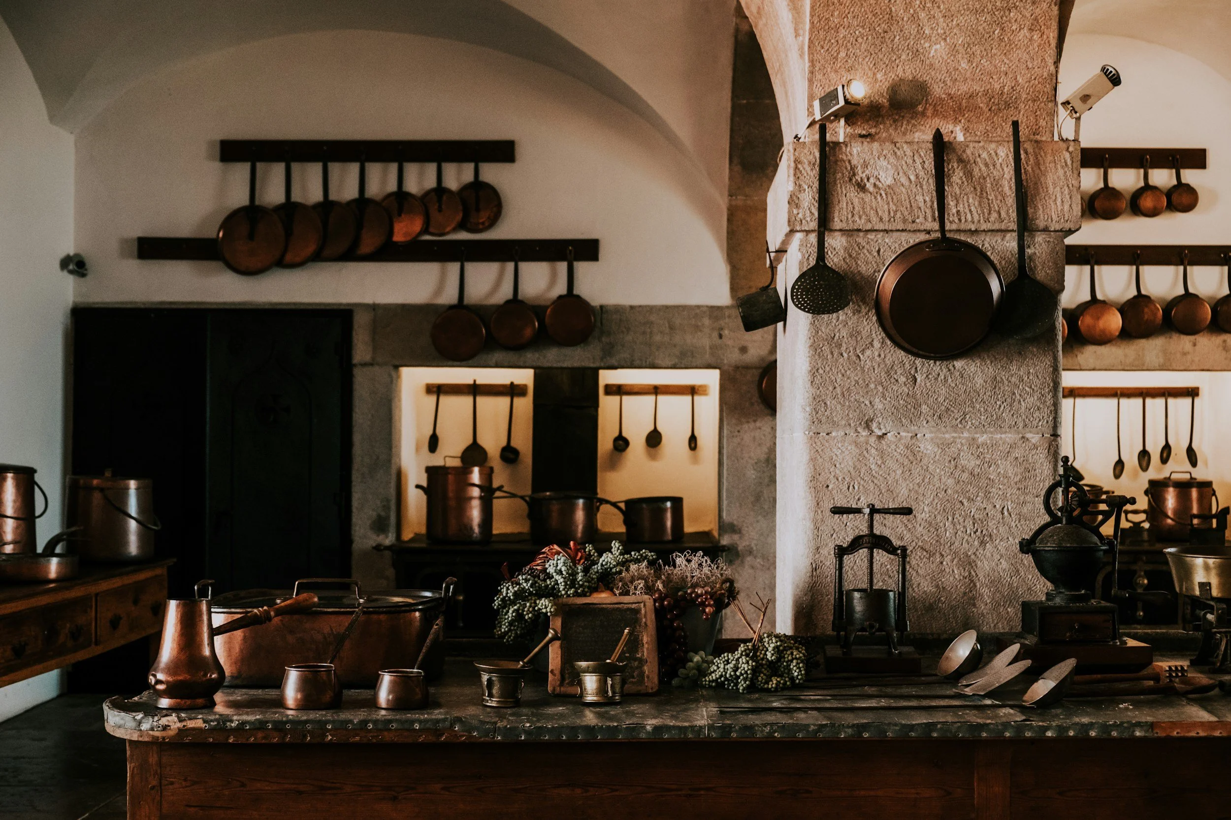 Rustic kitchen with hanging copper pots, a large wooden table, and vintage kitchen tools.