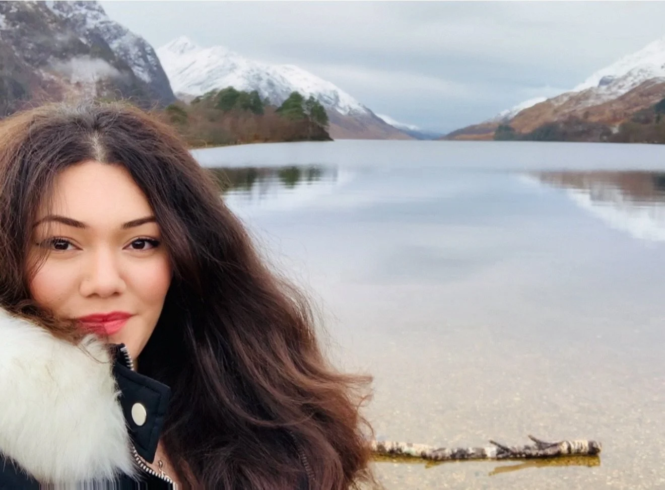 Daughter of Yore founder, Jade. A woman with long dark hair smiling near a calm lake with snow-capped mountains in the background.