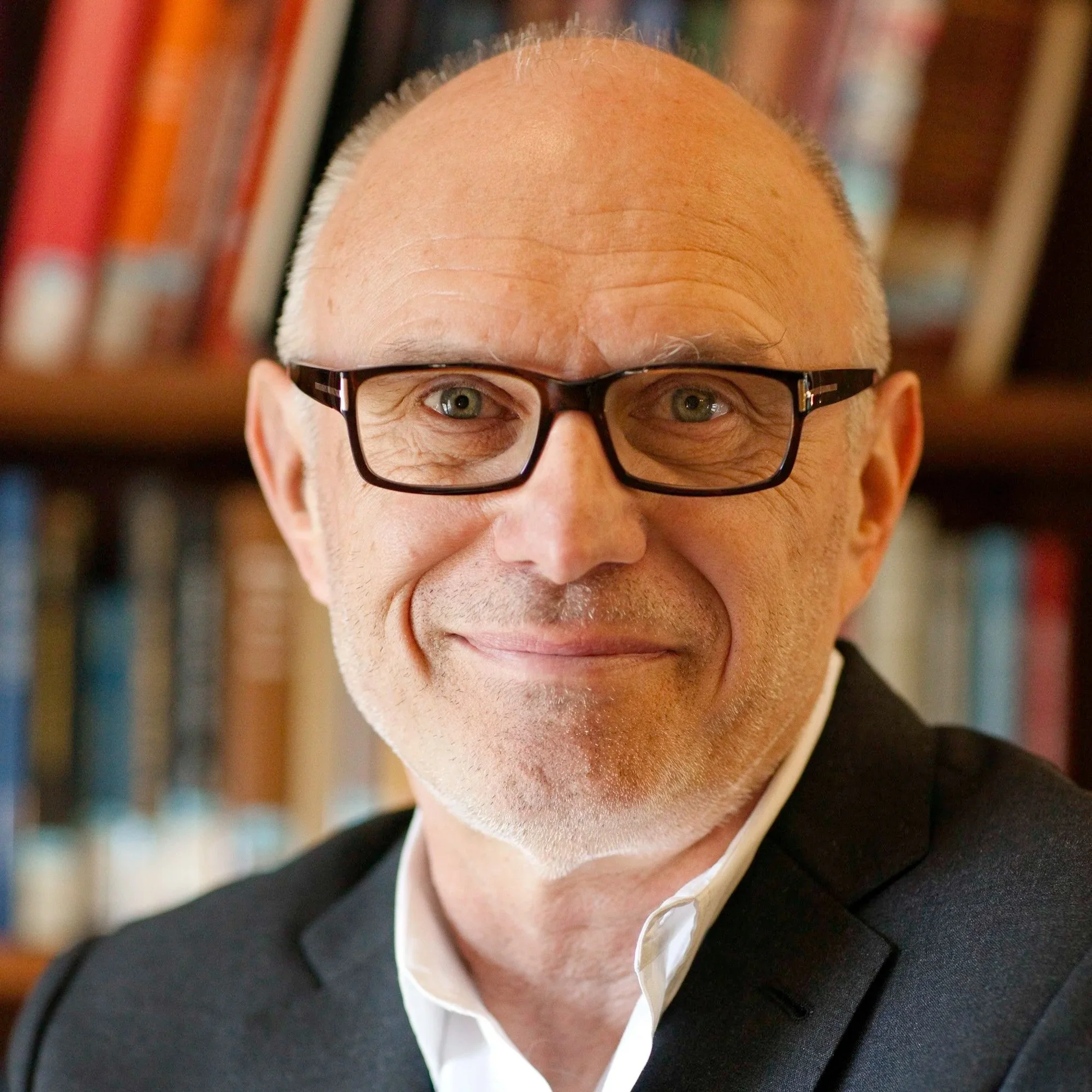 Portrait of a middle-aged man with glasses, smiling, with a bookshelf in the background.