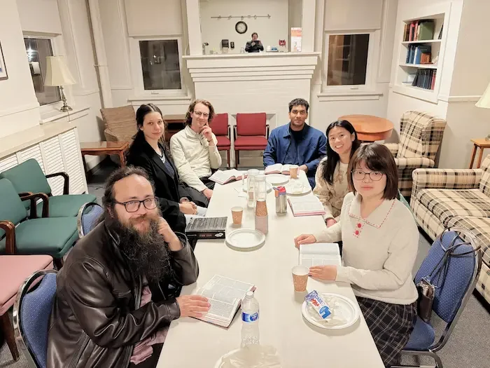 Group of people sitting around a table outdoors, engaged in conversation.