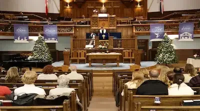 People seated in a church with a decorated altar and Christmas trees, attending a service or event.