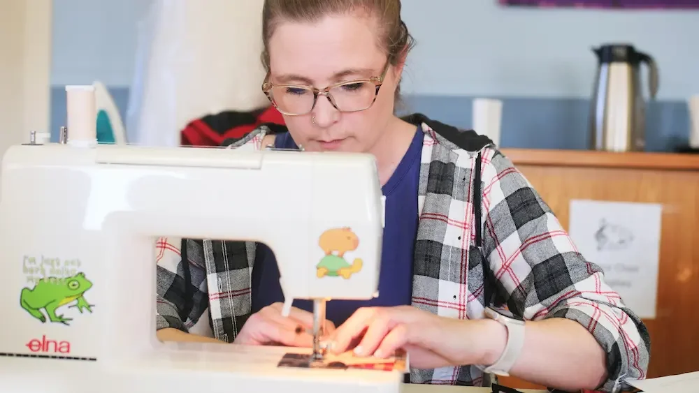 Young woman sewing on a white sewing machine with animal stickers at a table.