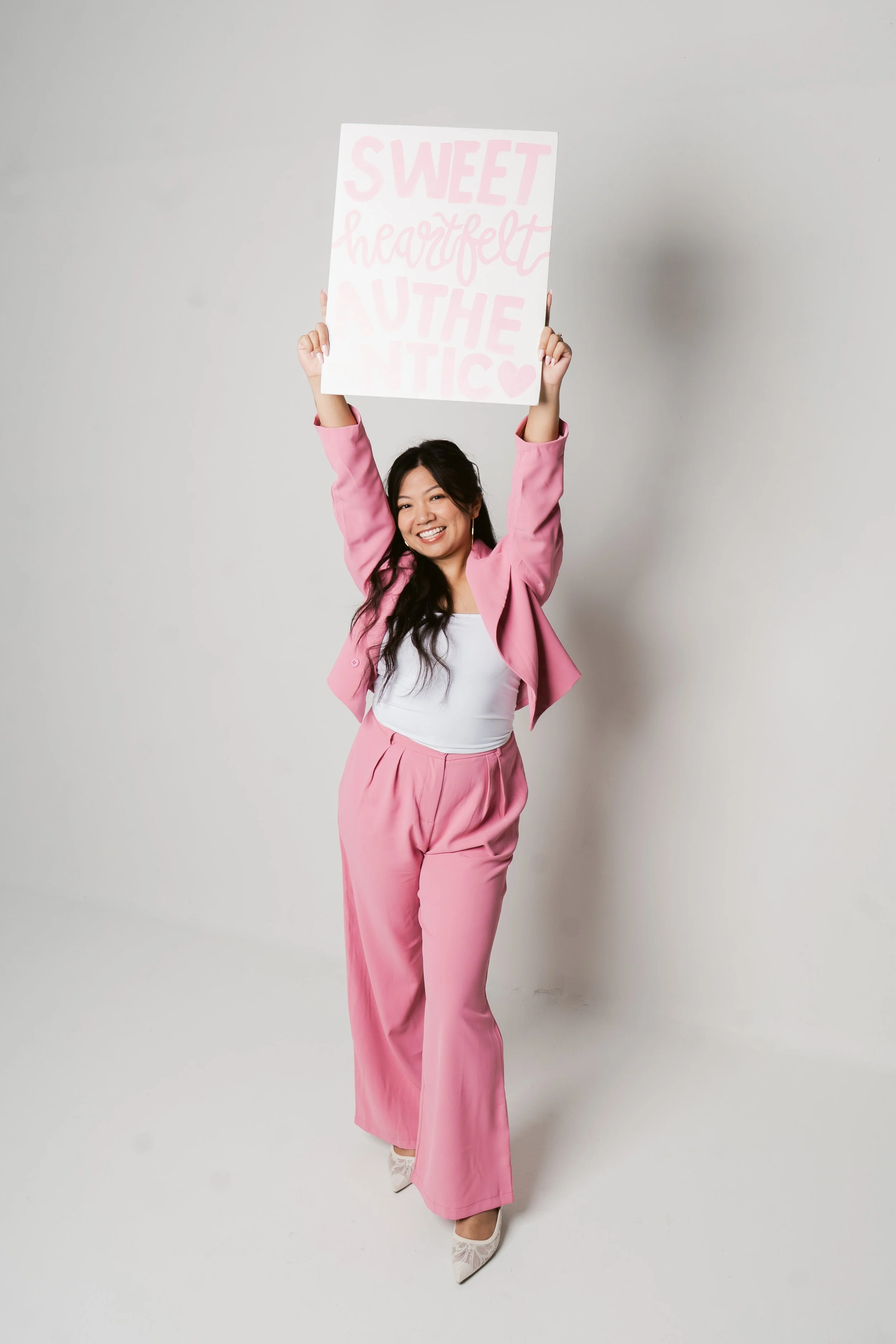 Smiling woman in pink suit holding a sign with the words "Sweetheart, you are iconic" written on it.