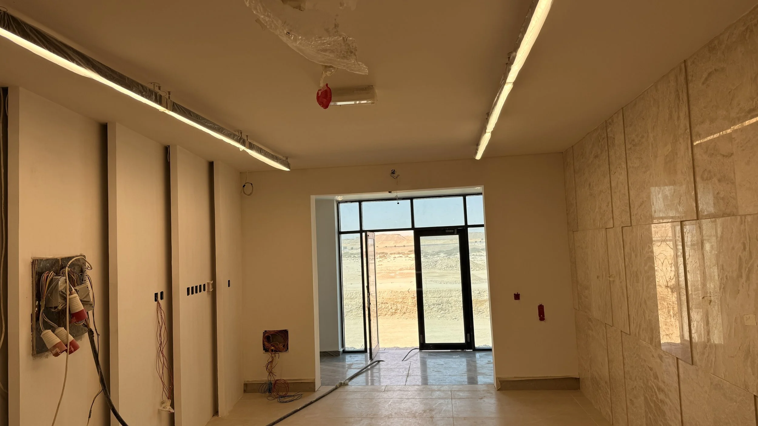 Interior of a building under construction with electrical wiring and outlets installed, a large window and doorway leading outside, and walls covered .residences oman, freehold, apartments visa residency muscat residences in duqm