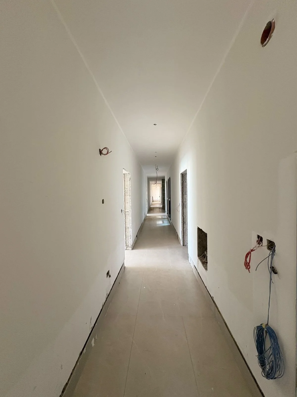 Long hallway Residences Oman Duqm under construction with electrical wires protruding from the walls and ceiling.