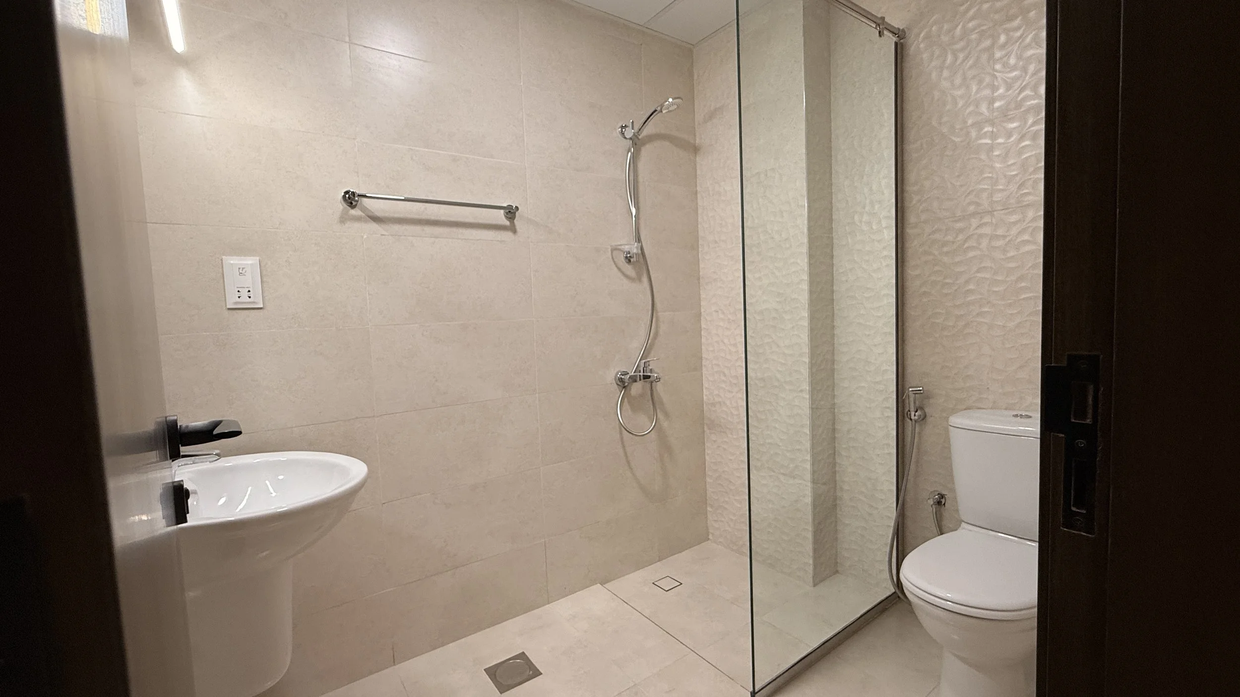 Bathroom with a walk-in shower, a toilet, a small sink, a towel rack, and a wall-mounted faucet, all in neutral colors..residences oman, freehold, apartments visa residency muscat residences in duqm