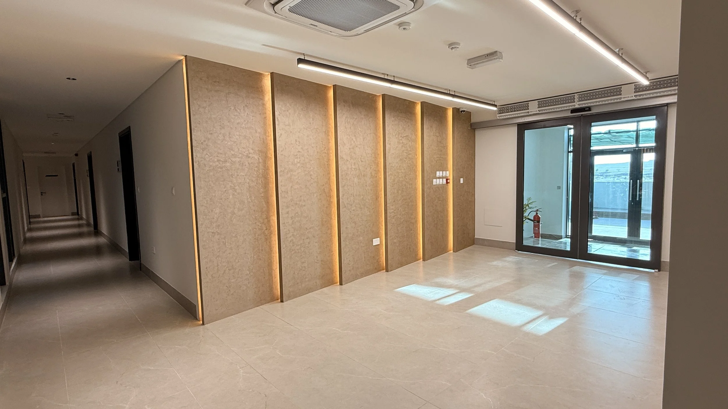 Modern interior hallway with a feature wall with vertical lighting accents, large windows, and tiled flooring.
