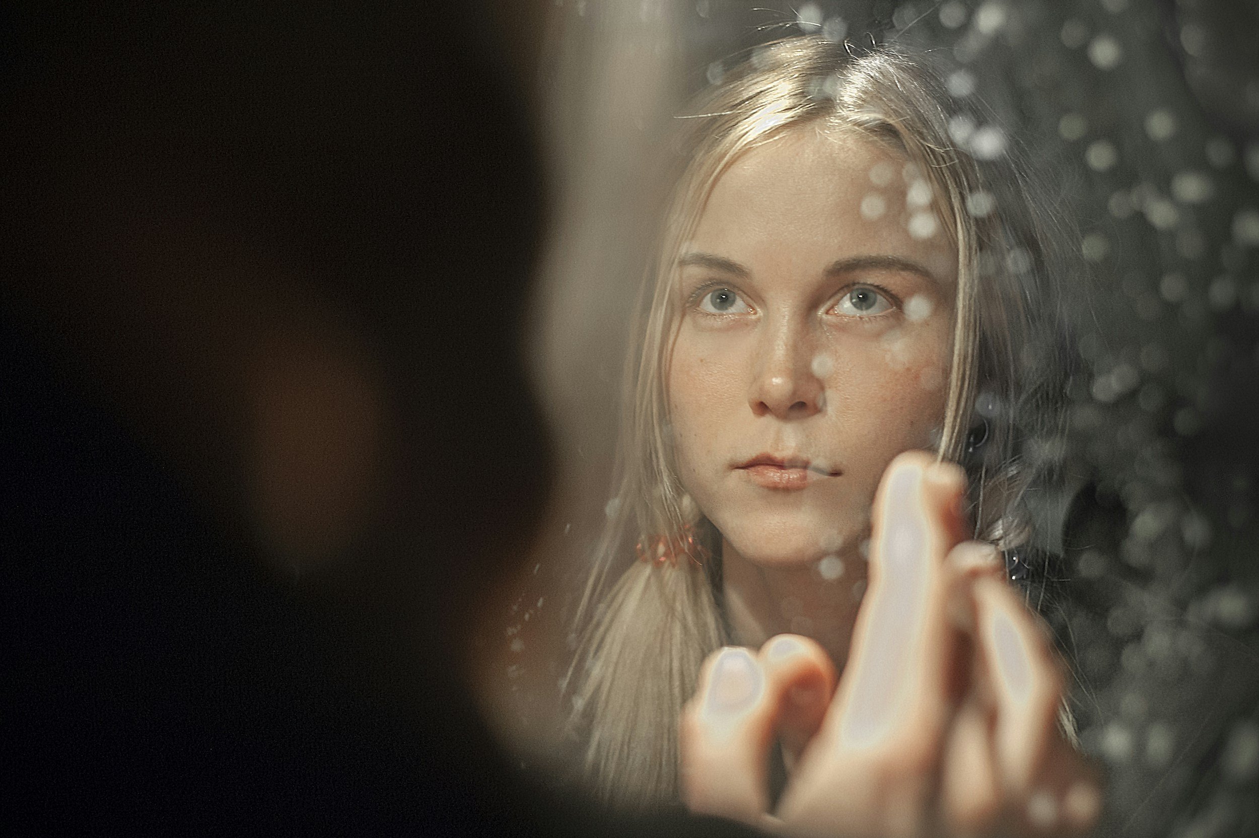 Woman looking at her reflection with her fingertips touching a spotted mirror.