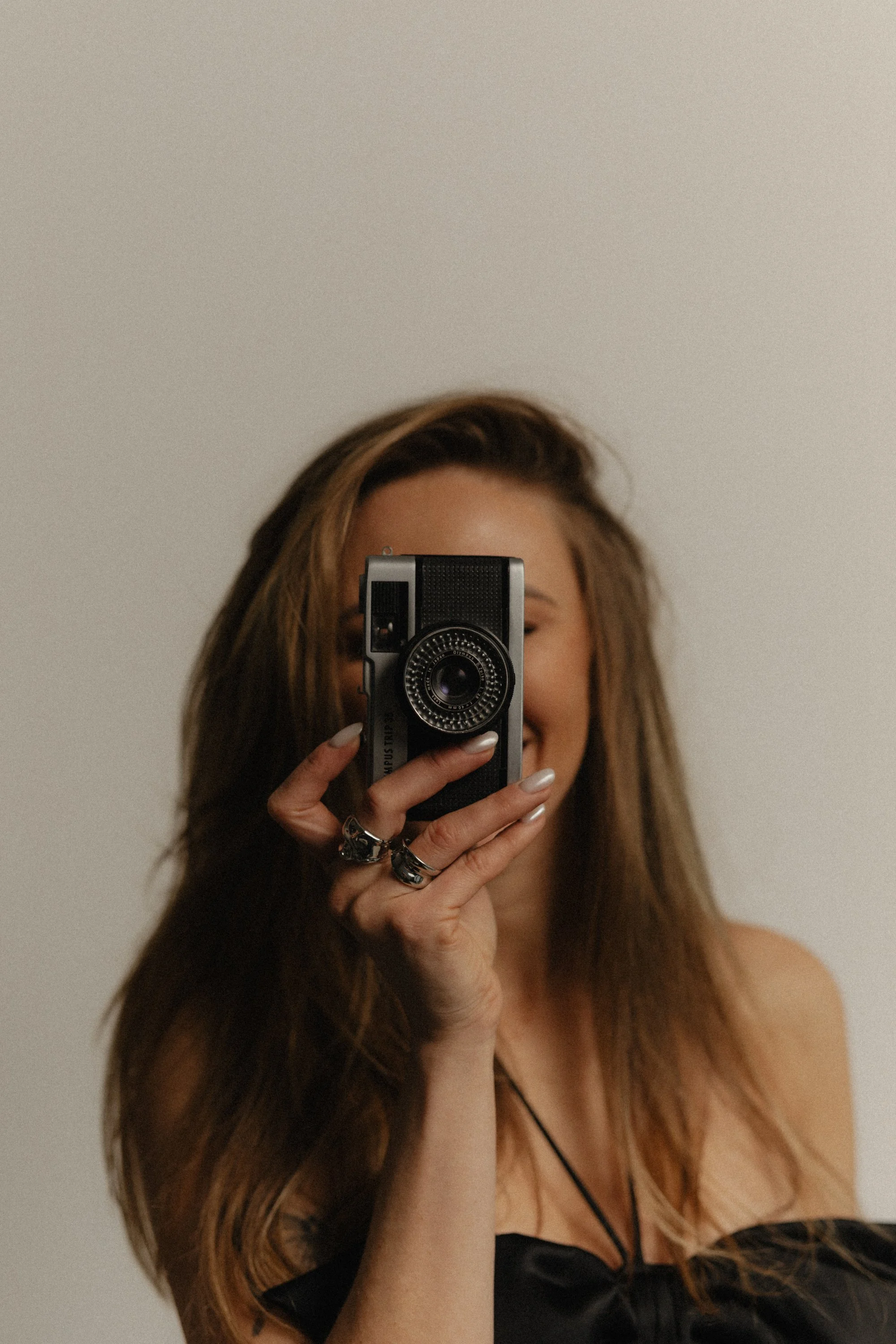 Premium Squarespace Template, Coaching Squarespace Template, Avelã Creative. Person holding a vintage camera in front of their face, smiling, with long hair and wearing rings.