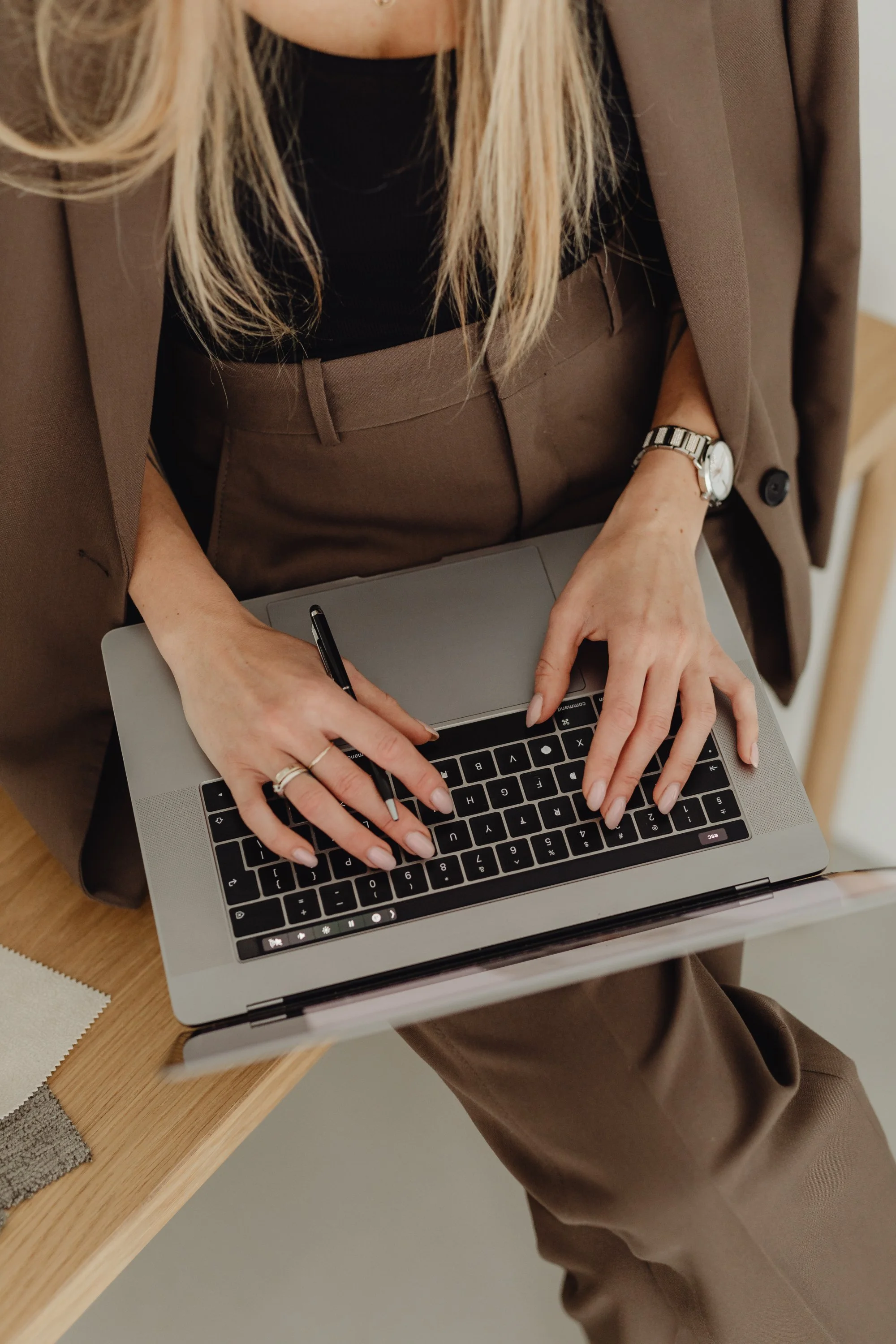 Premium Squarespace Template, Coaching Squarespace Template, Avelã Creative. Woman in brown suit typing on a laptop, seated at a wooden desk, holding a pen.