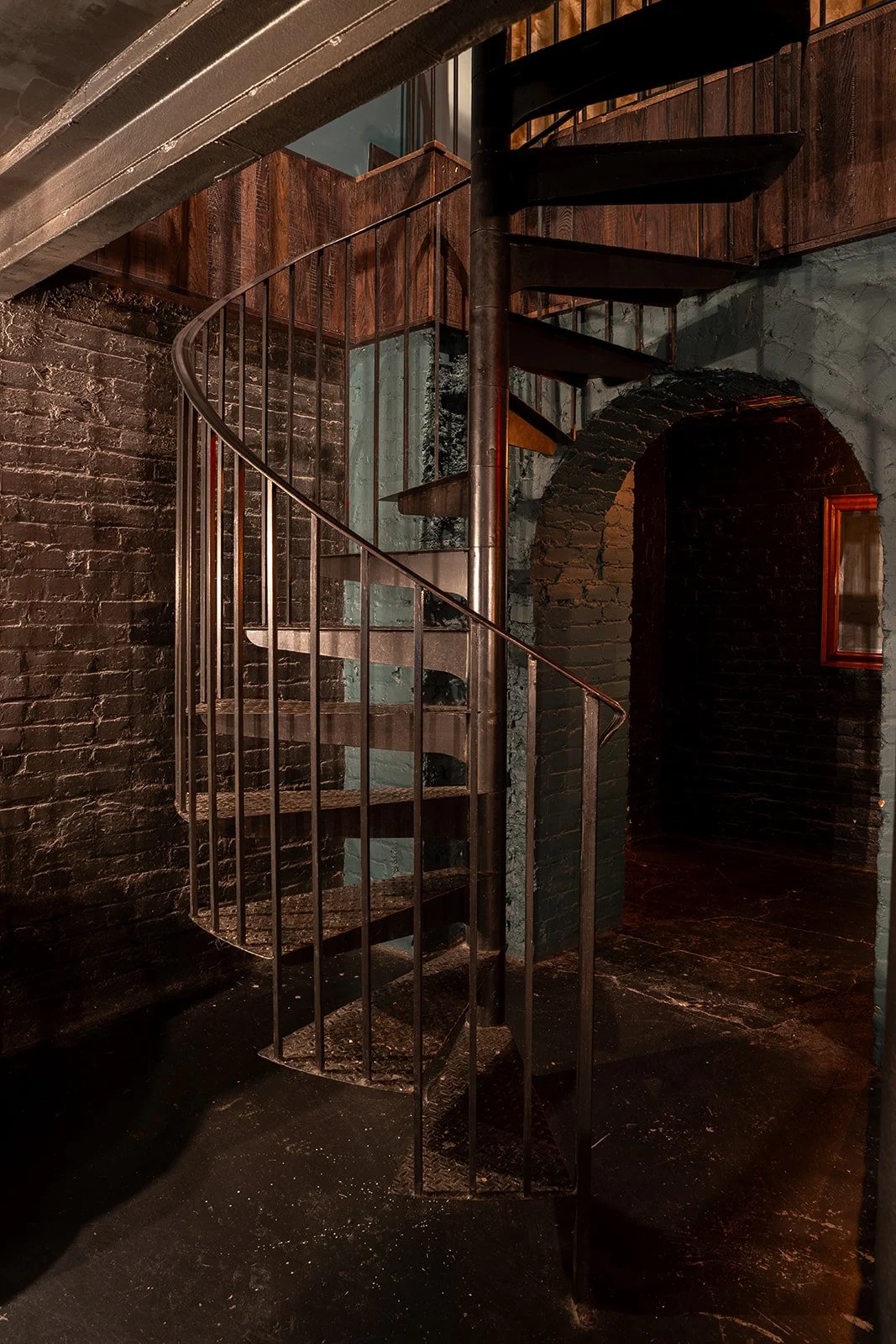 Interior of a building with a metal spiral staircase, brick walls, wooden accents, and a arched doorway.