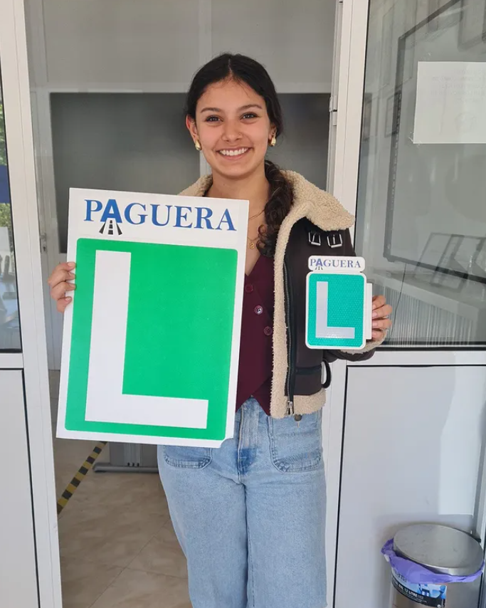 Una joven sosteniendo signos de aprendizaje para conducir en una oficina de tránsito, con una sonrisa en su rostro.