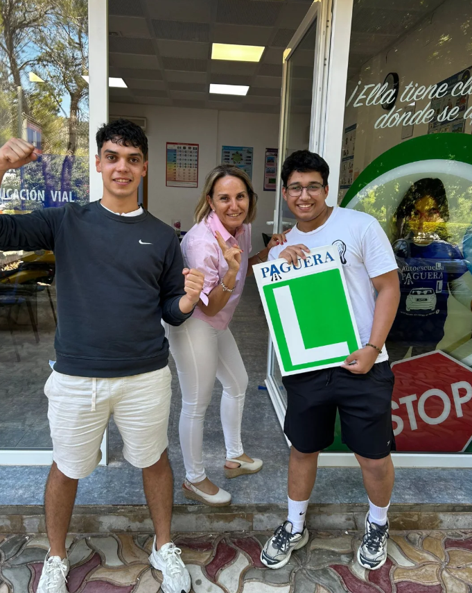 Tres personas en la entrada de una autoescuela, una de ellas con una señal de aprendizaje con la letra 'L', y otra con una actitud de celebración.
