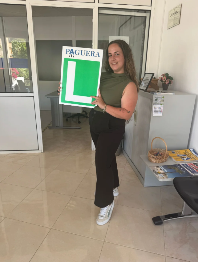 Mujer sosteniendo letrero de Paguera con una letra grande en verde y la palabra Paguera en la parte superior.