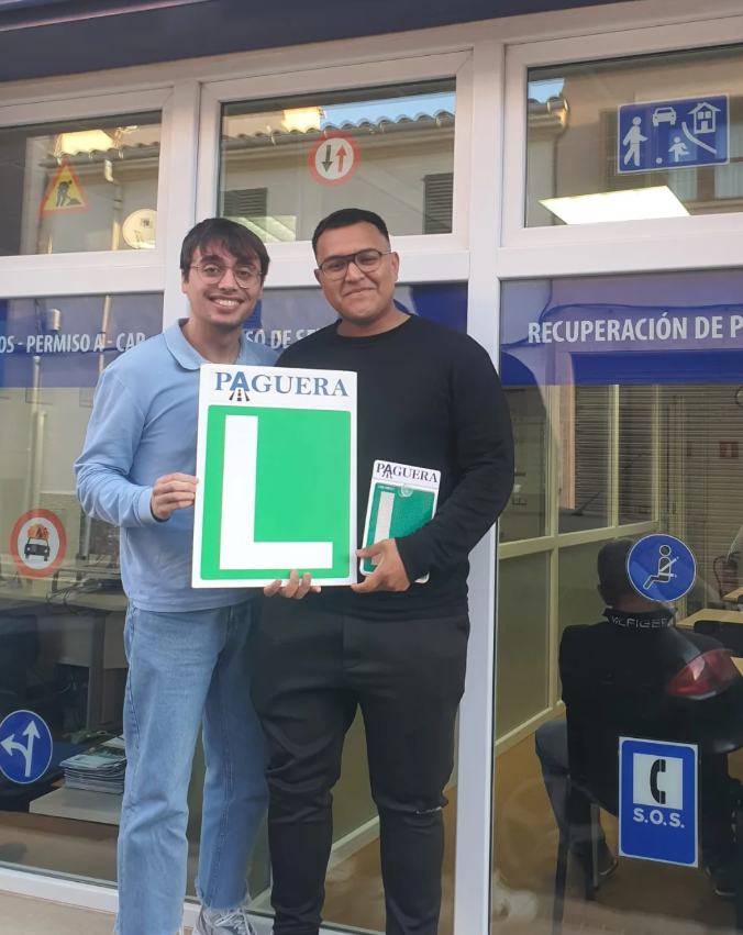 Dos hombres sonriendo y sosteniendo señales de aprendizaje de manejo. Están en un centro de educación vial.