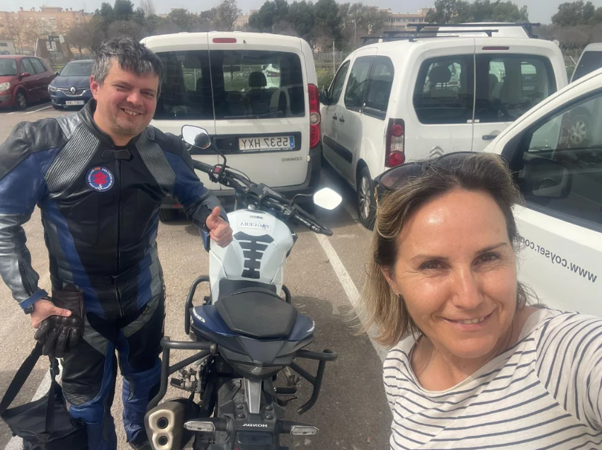 Una mujer tomando una selfie junto a un hombre con un equipo de motocicleta en un estacionamiento.