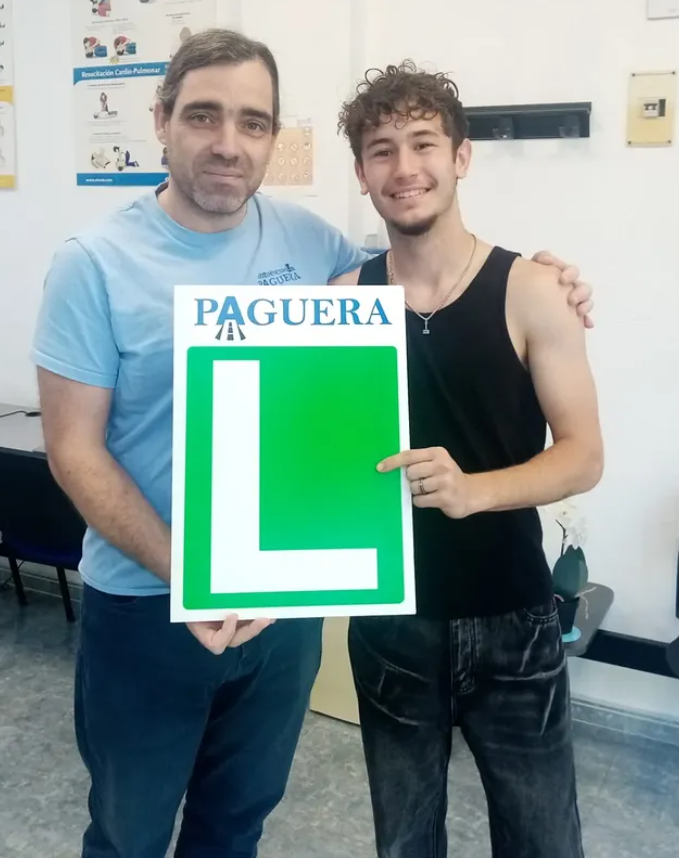 Dos hombres sosteniendo una señal que dice 'PAGUERA' en la parte superior y muestra la letra 'L' grande en verde.