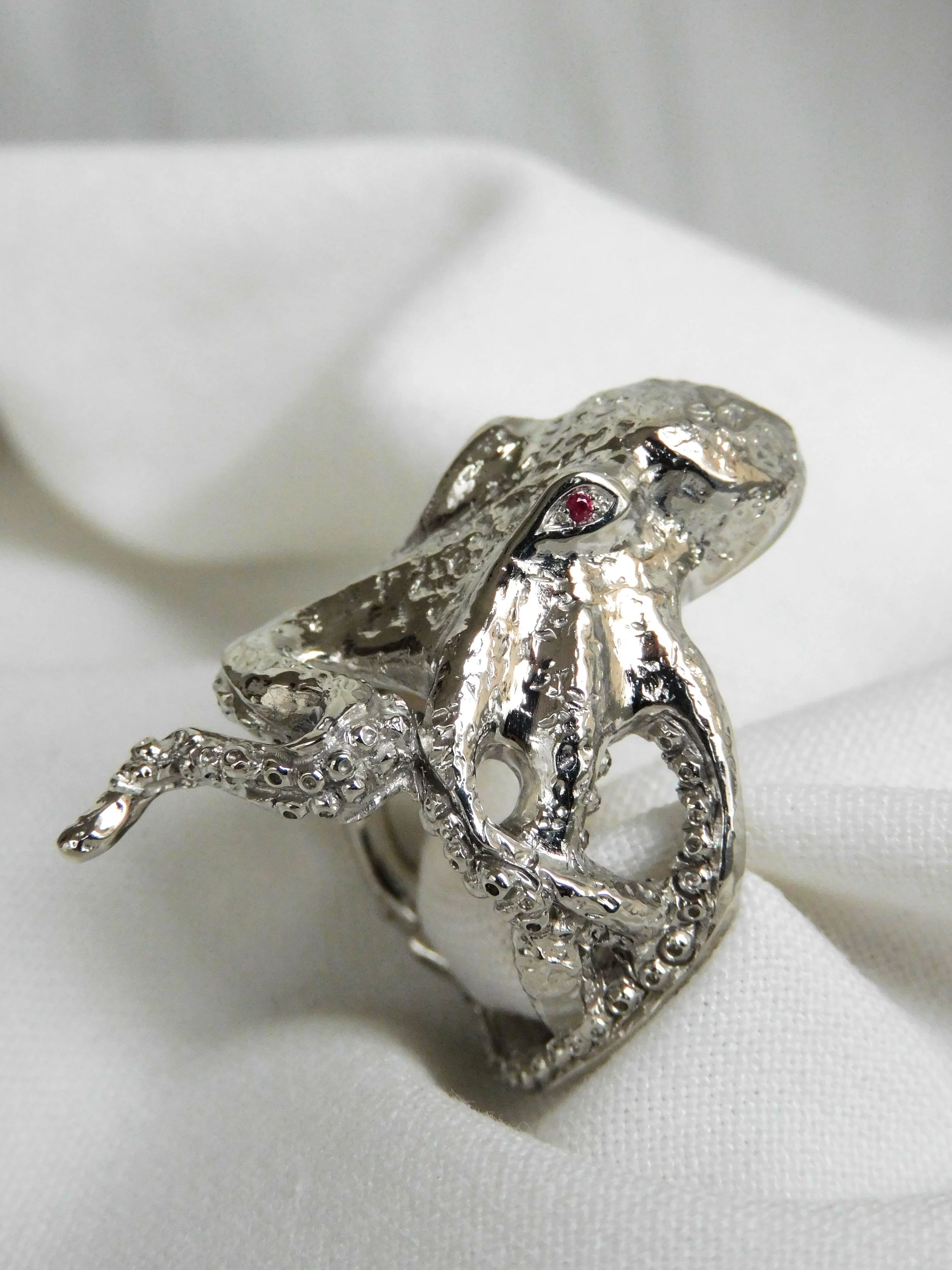Bague en argent 925 en forme de pieuvre avec une pierre rouge pour les yeux, posée sur un tissu blanc.