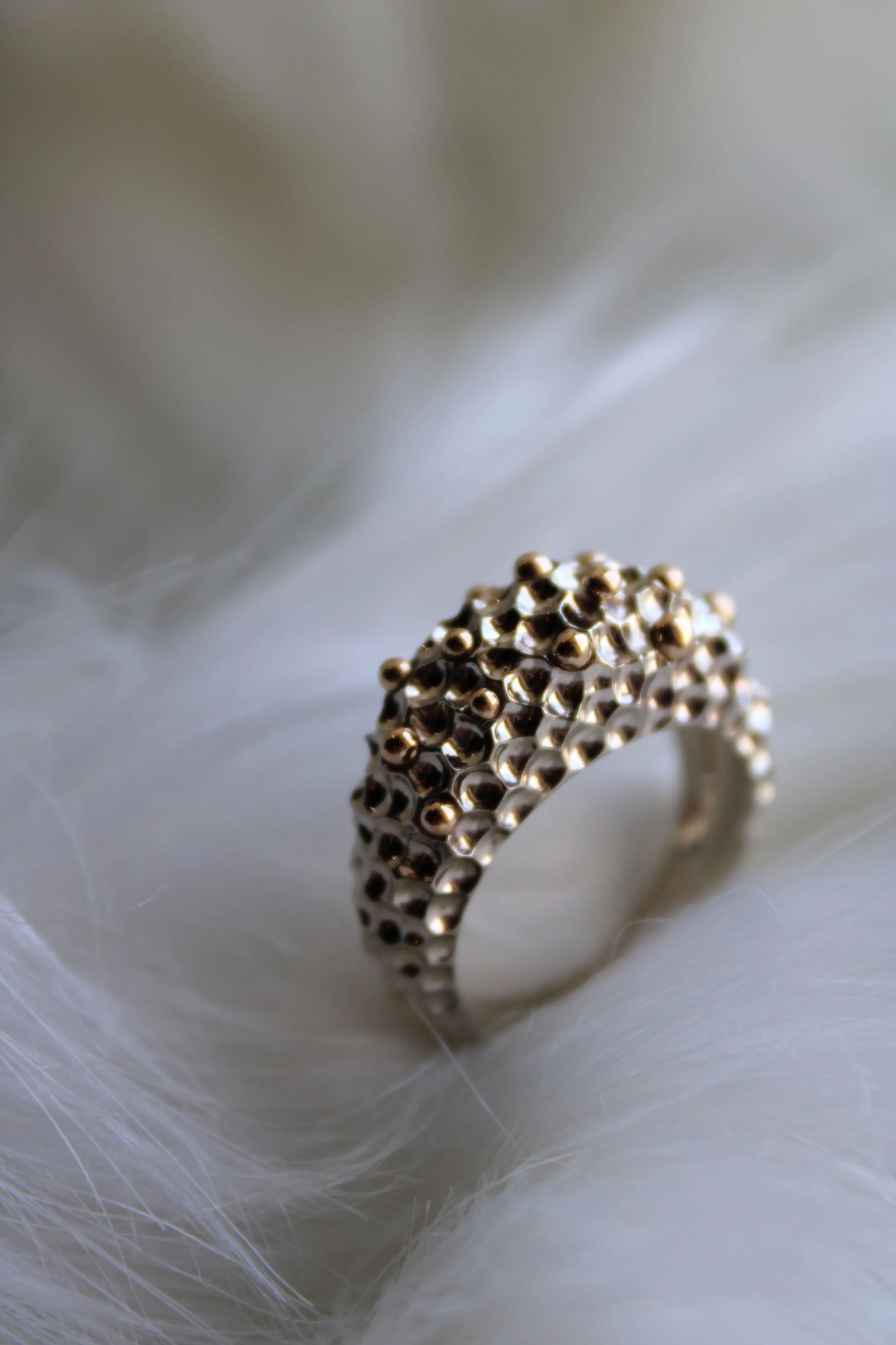 Bague dorée martelée ornée de petites boules dorées, posée sur une surface blanche.