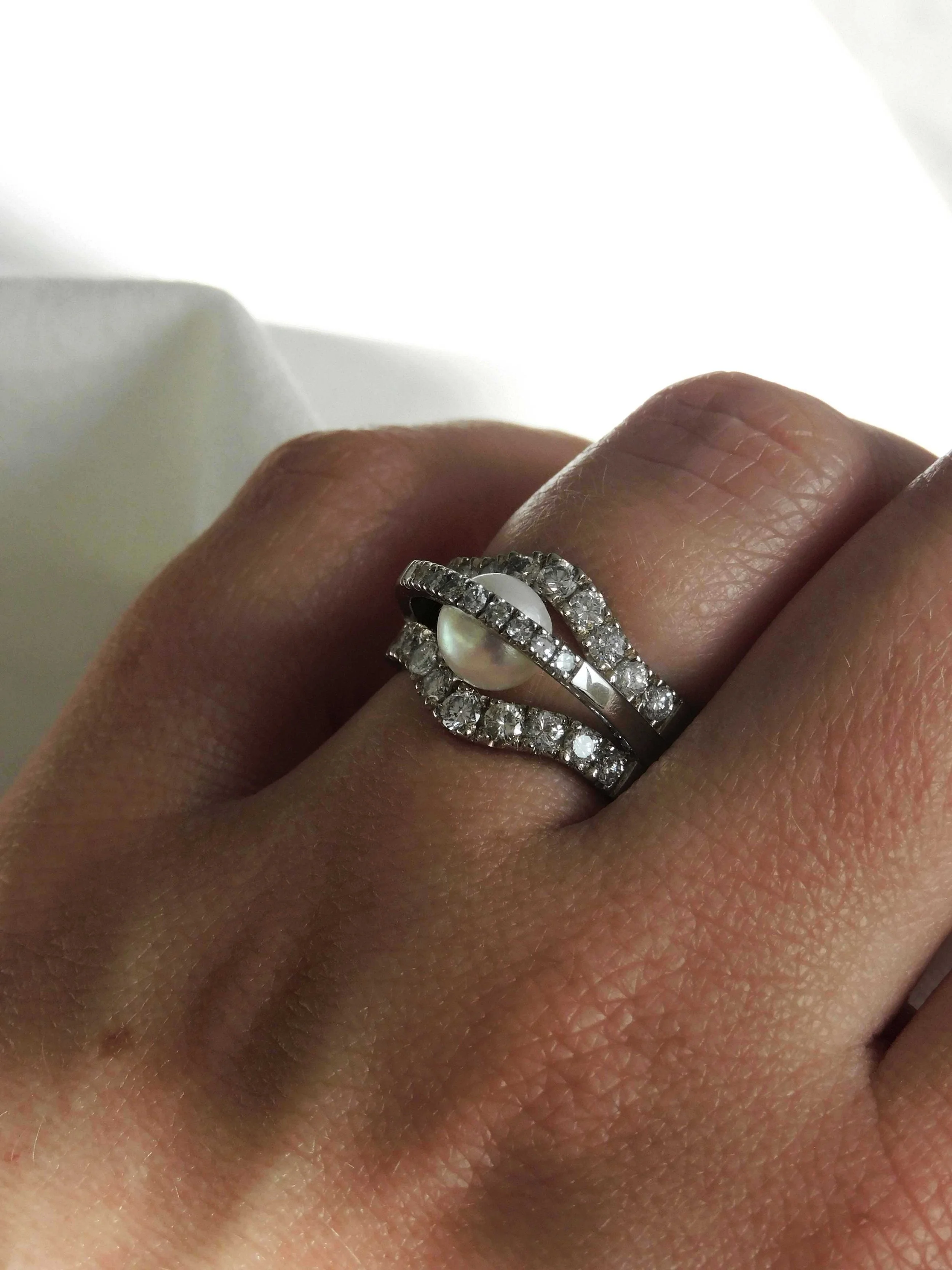 Une main portant une bague en argent 925 orné de nombreux diamants et d'une perle au centre.