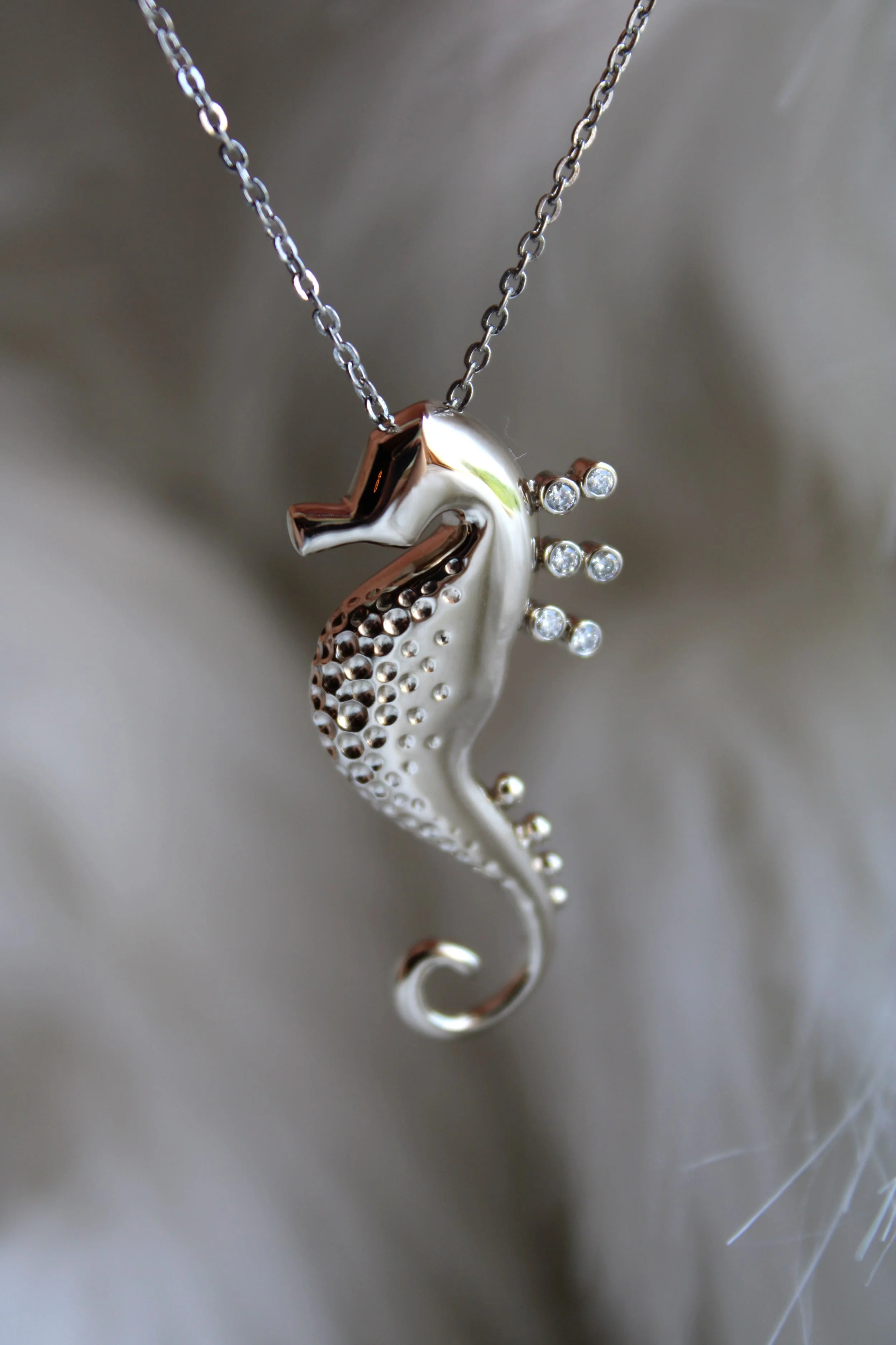Collier avec pendentif en forme d'hippocampe en métal argenté avec petites pierres brillantes.