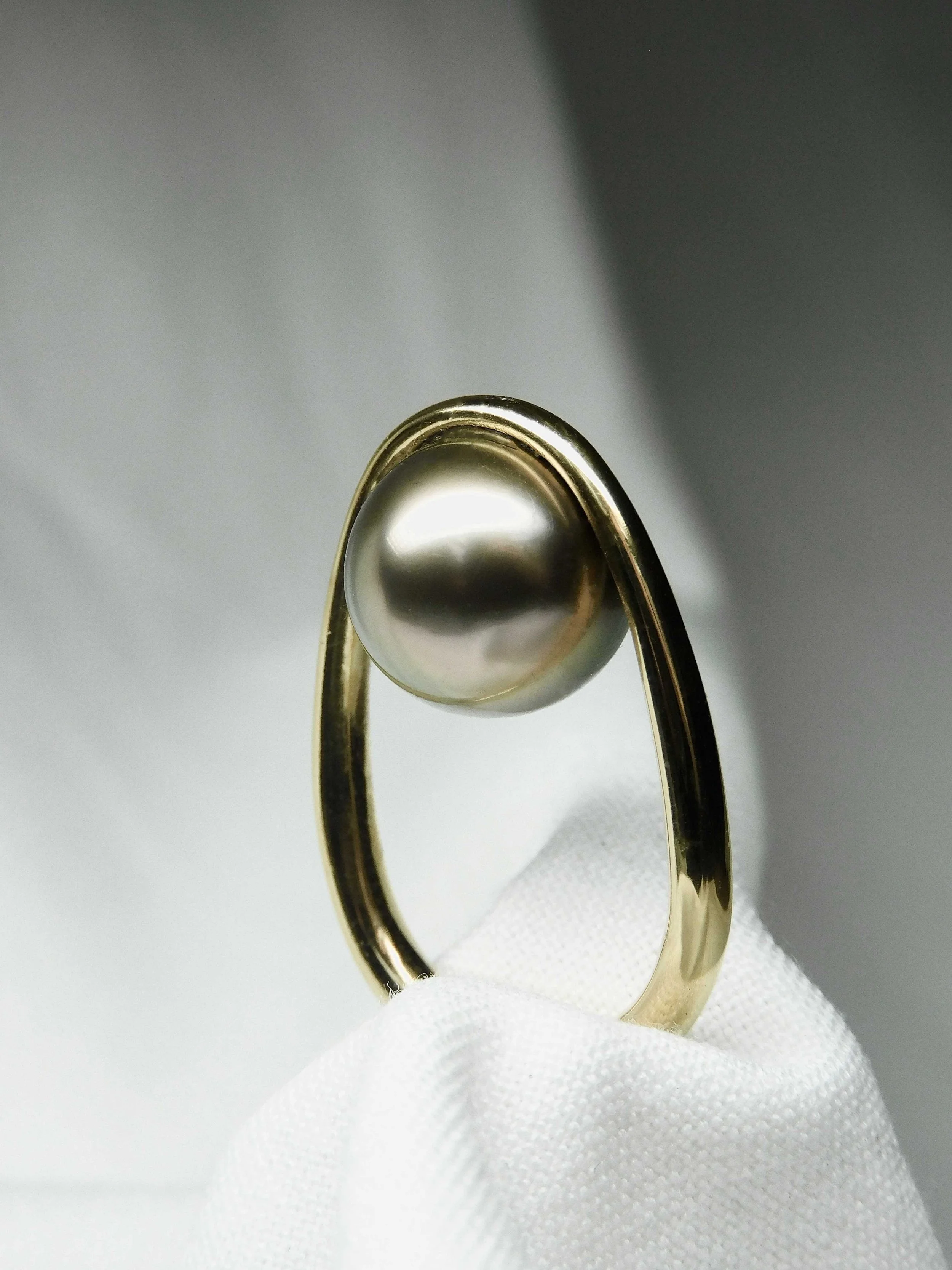 bague ovale dorée avec une perle à l'intérieur de l'anneau, posée sur un tissu blanc.