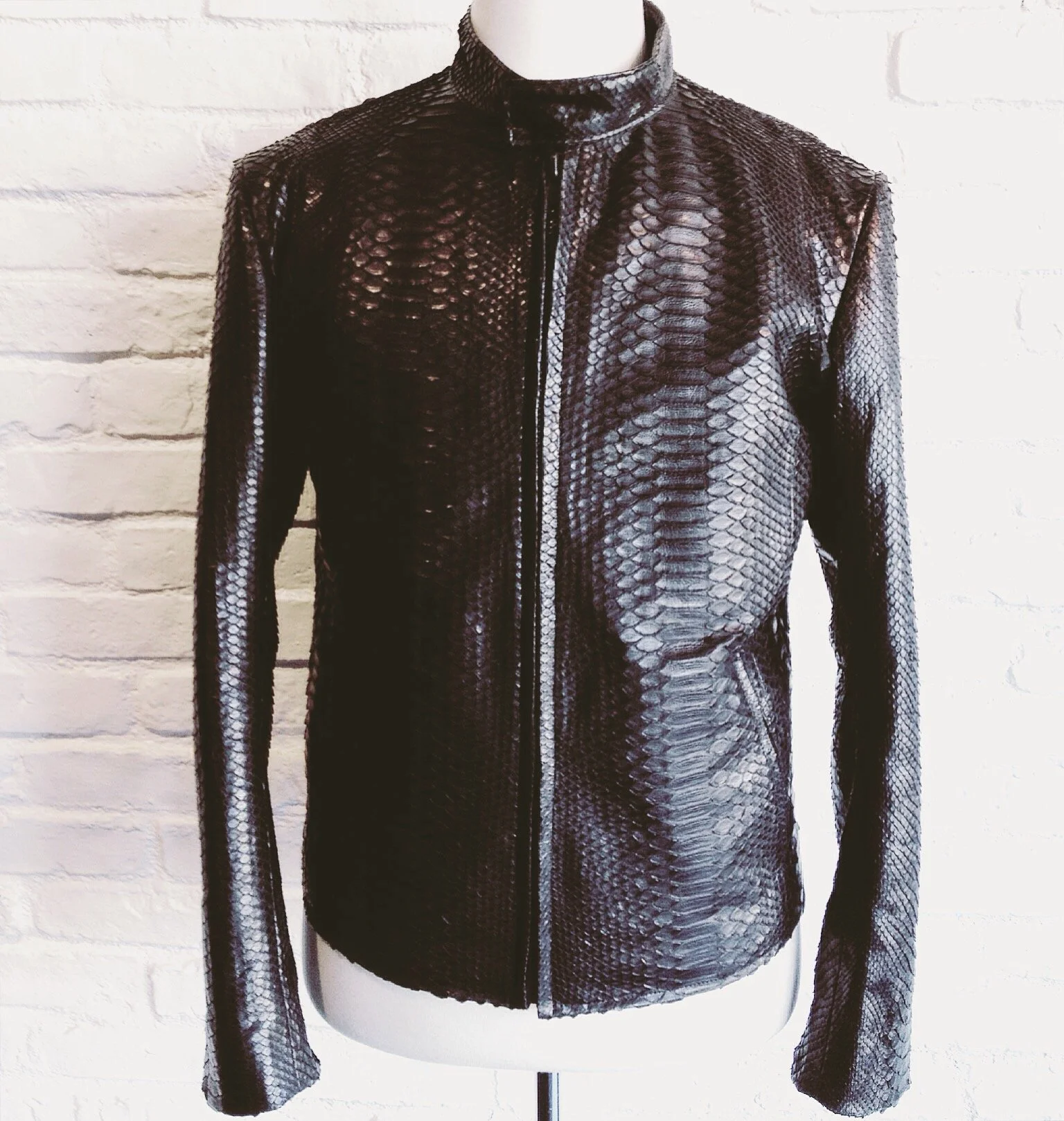 Black snakeskin-patterned jacket on a mannequin, set against a white brick wall background.