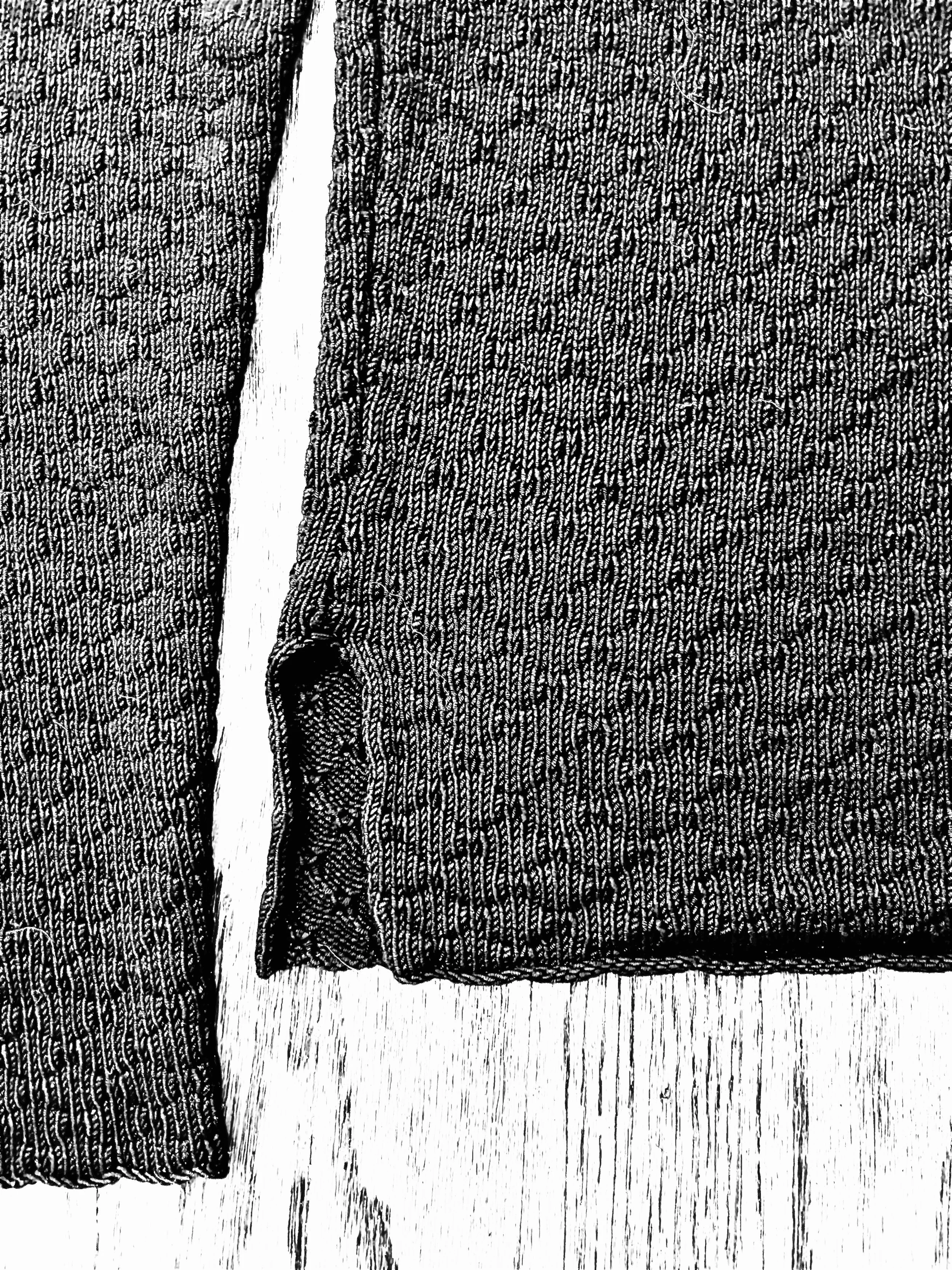 Close-up of a pair of denim jeans with a tear along the seam, lying on a wooden surface.