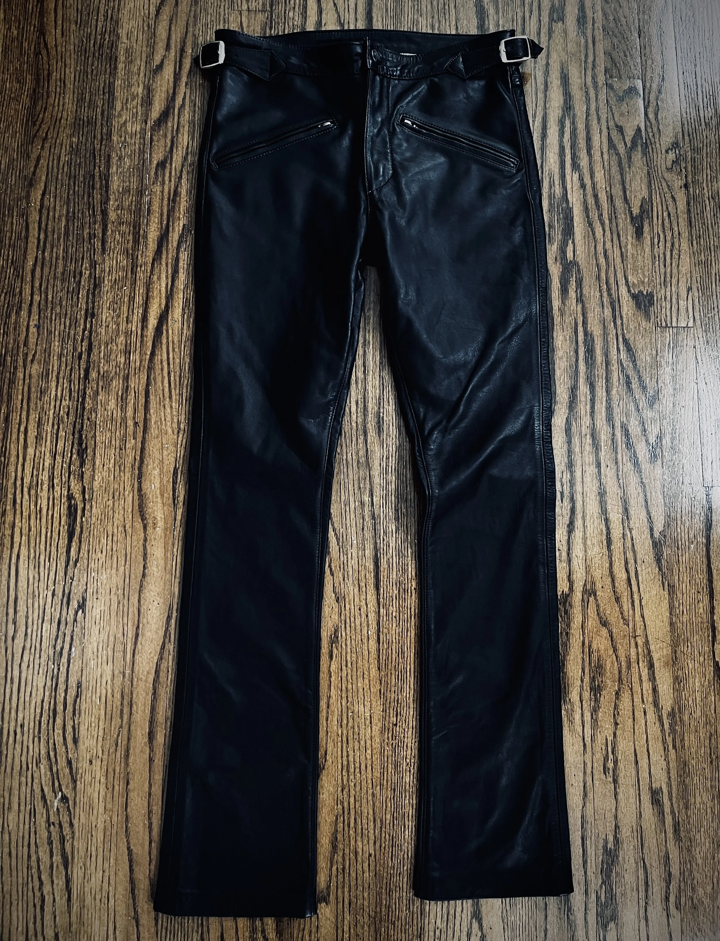 Black leather pants with zippered pockets on a wooden floor
