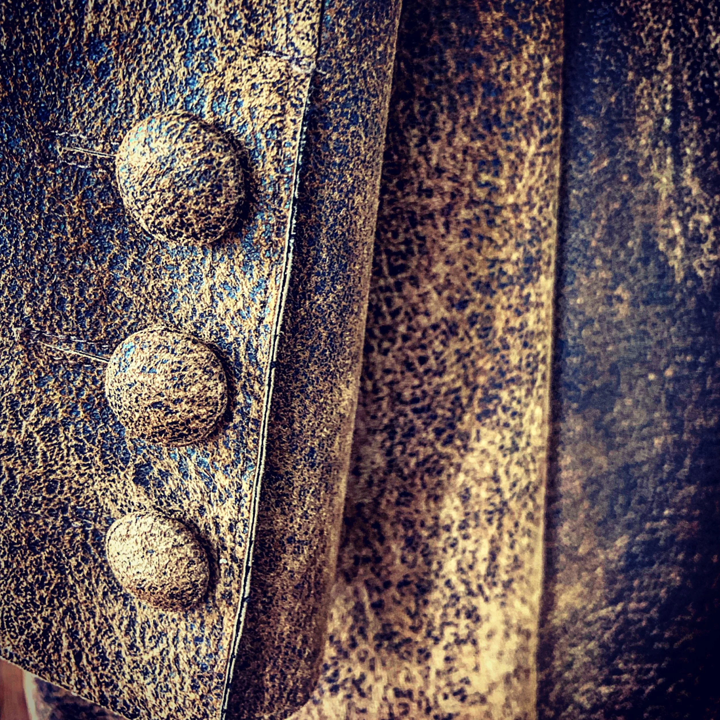 Close-up of a textured, rust-colored metal surface with three metallic, rounded knobs.