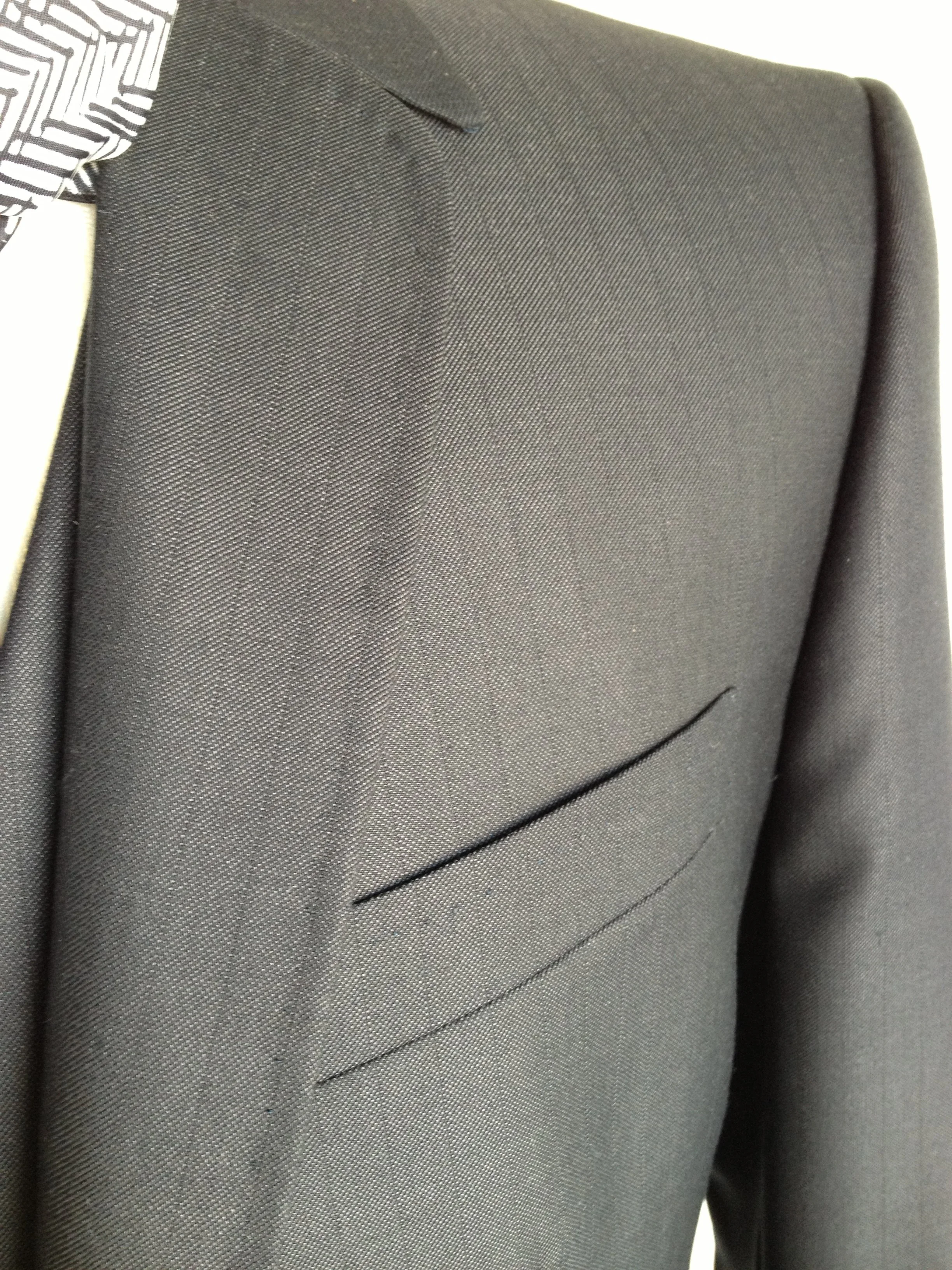 Close-up of a gray suit jacket with a white shirt and a black-and-white patterned tie.