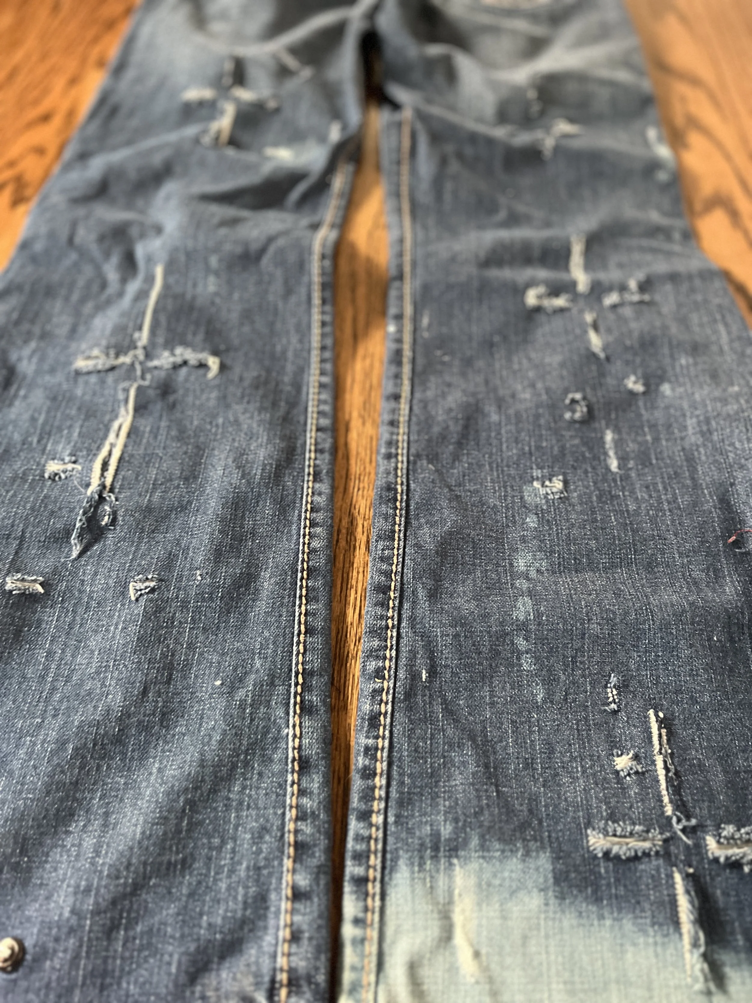 A pair of distressed, ripped denim jeans laid flat on a wooden surface.