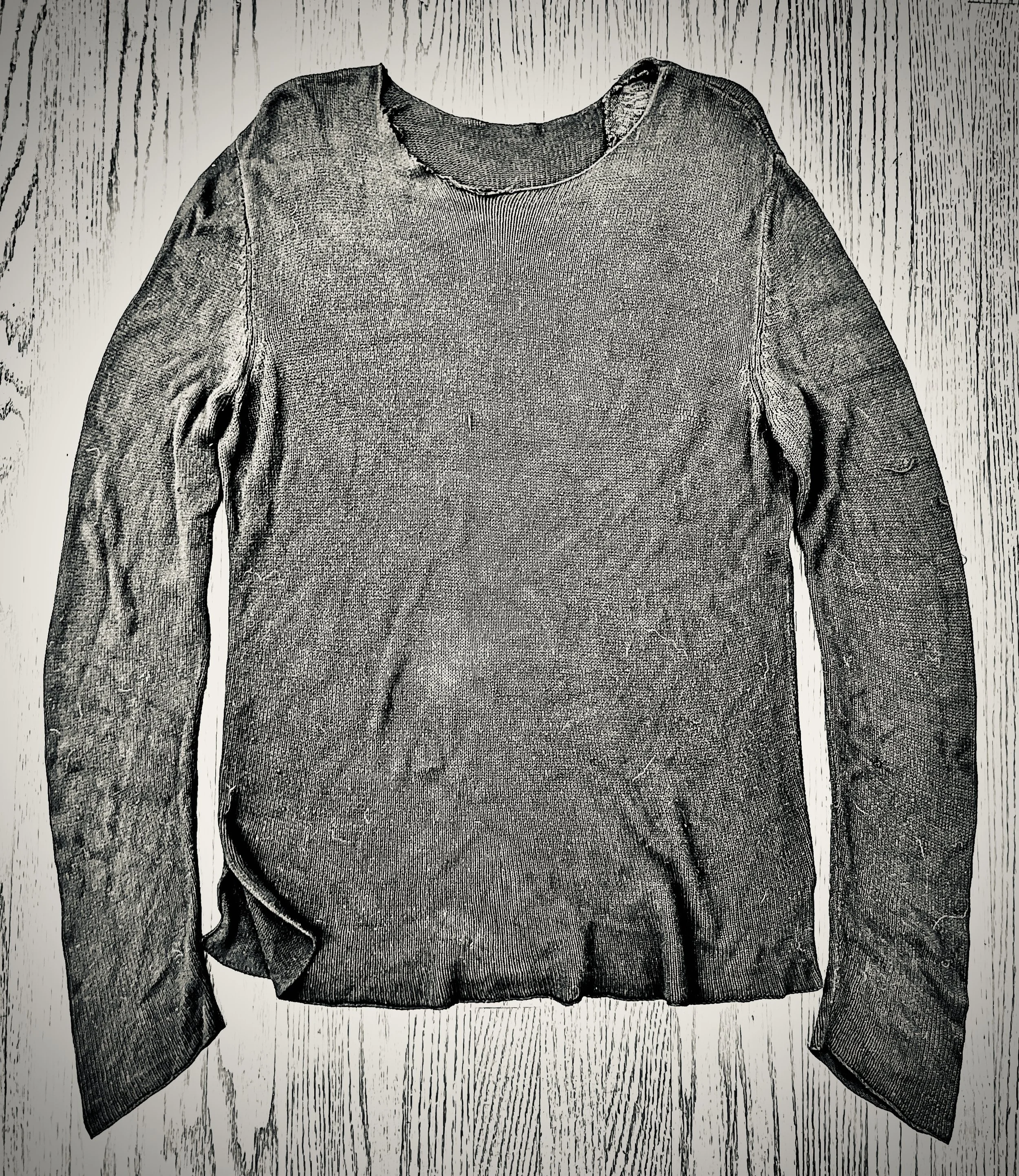 A worn, gray long-sleeve sweater with a distressed neckline, laid flat on a wooden surface.