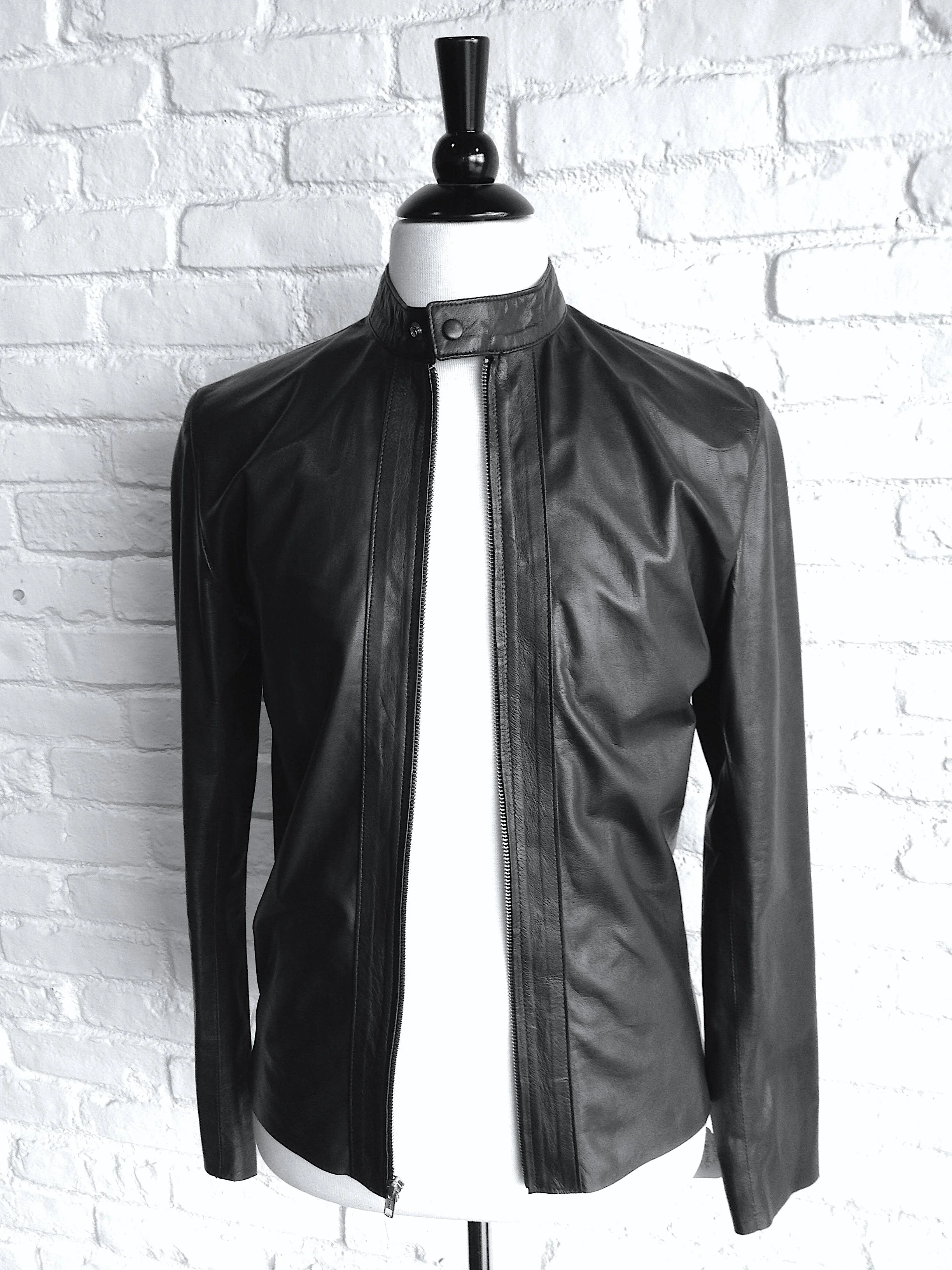 Black leather jacket displayed on a mannequin against a white brick wall
