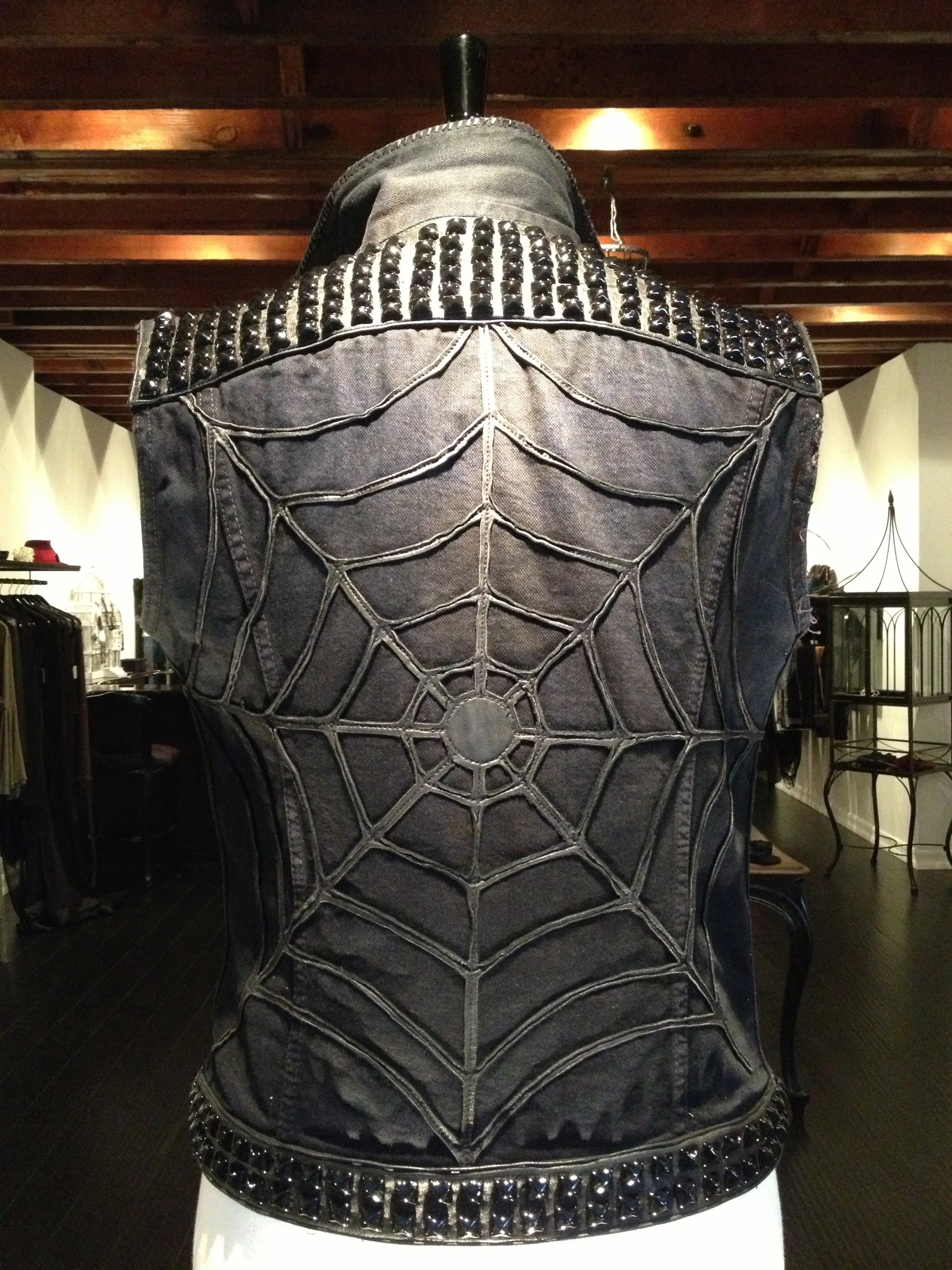 Back of a black vest with a large embroidered spider web design and studded shoulders.