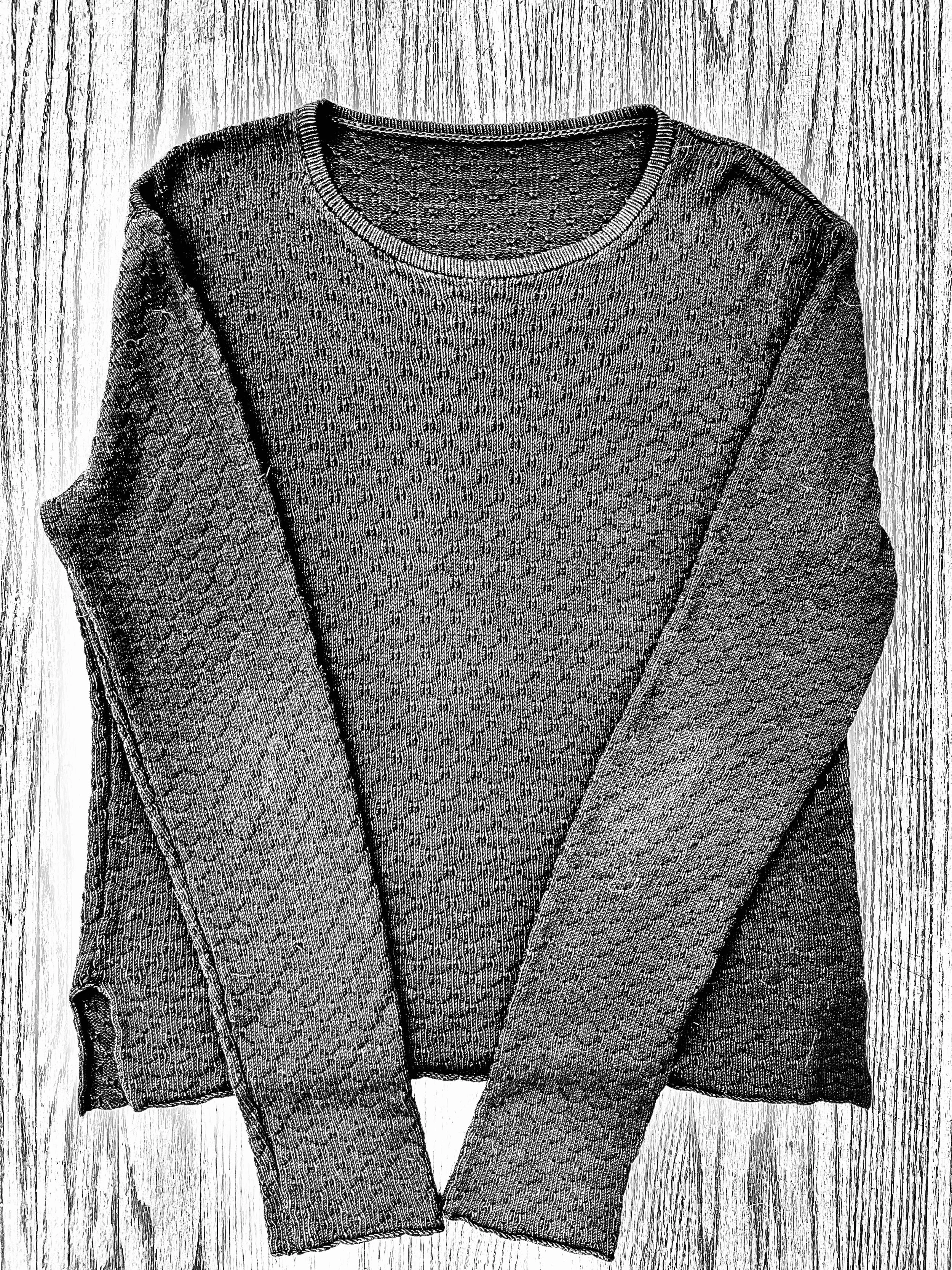 A long sleeve, textured sweater laid flat on a wooden surface.