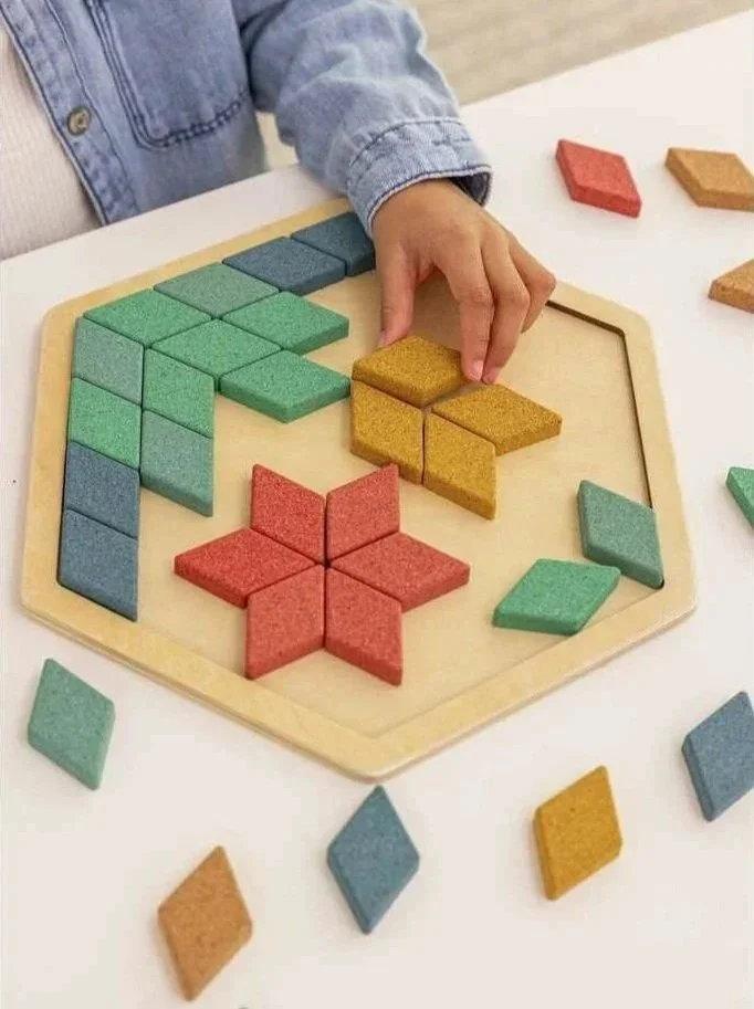 Child playing with colorful cork diamond shapes placed in a hexagonal wooden tray. By Korko.