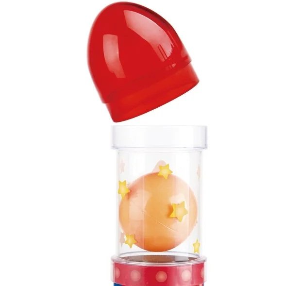 A red and white children's toy with a transparent cylinder containing orange balls and yellow star-shaped objects, with a red lid positioned above the container.