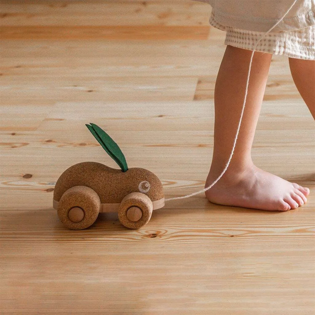 Child's foot with a car-like toy in the shape of a cork rabbit with soft green felt ears attached to a string. By Korko.