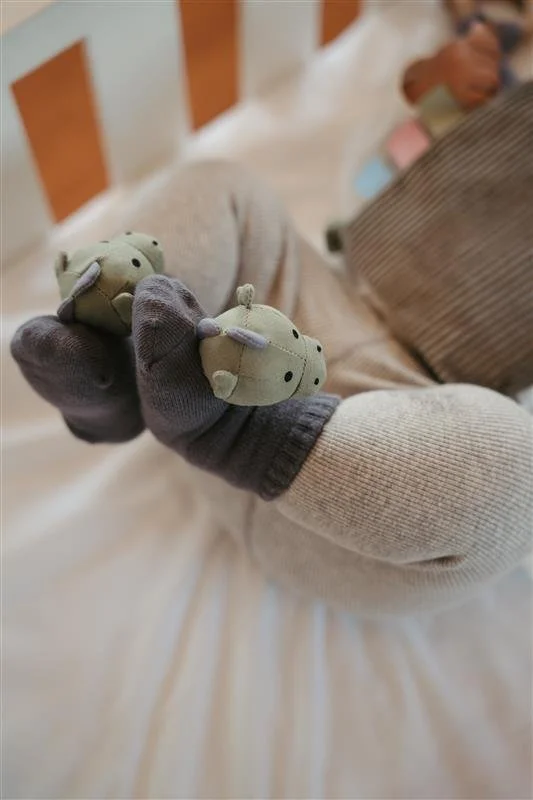 Person wearing dark gloves holding two small plush teddy bears with green and gray colors in hand.