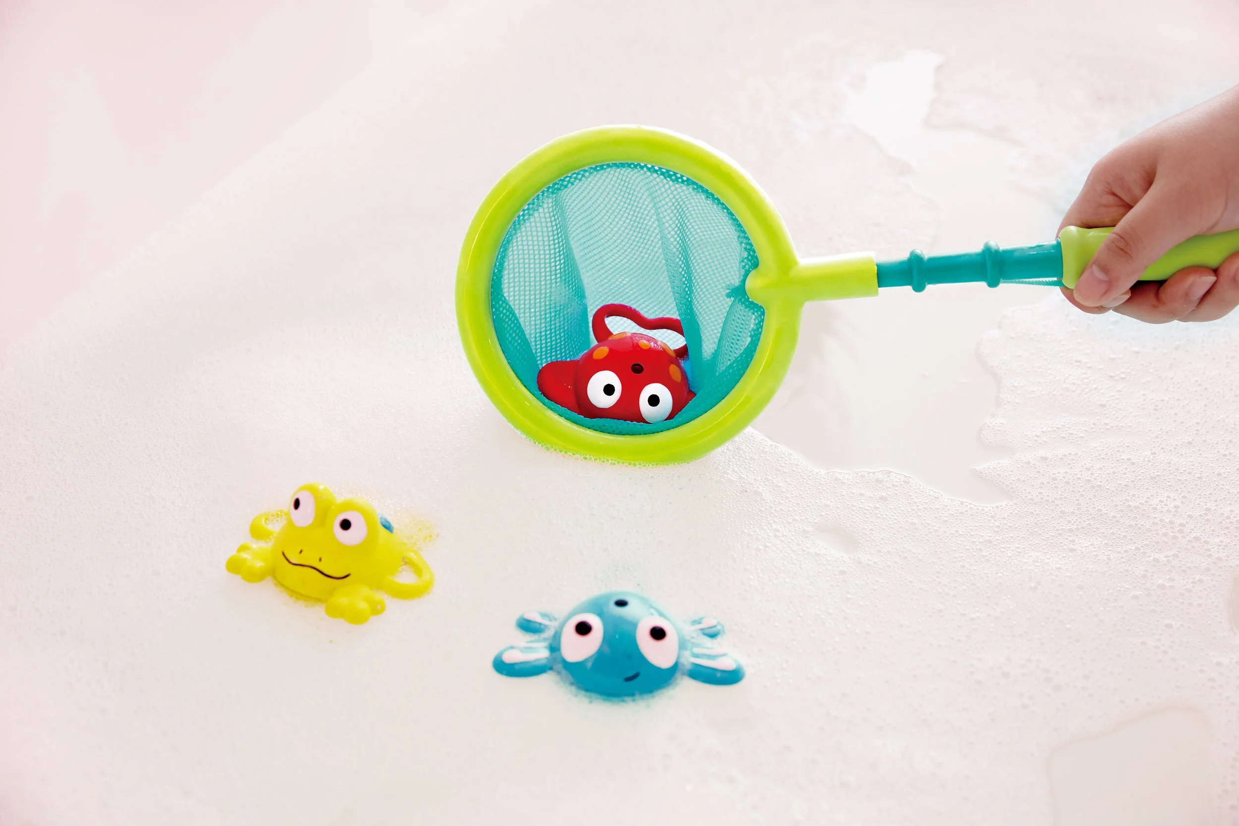 Child's hand holding "double Fun Fishing Set" by Hape and playing with it in the bathub.