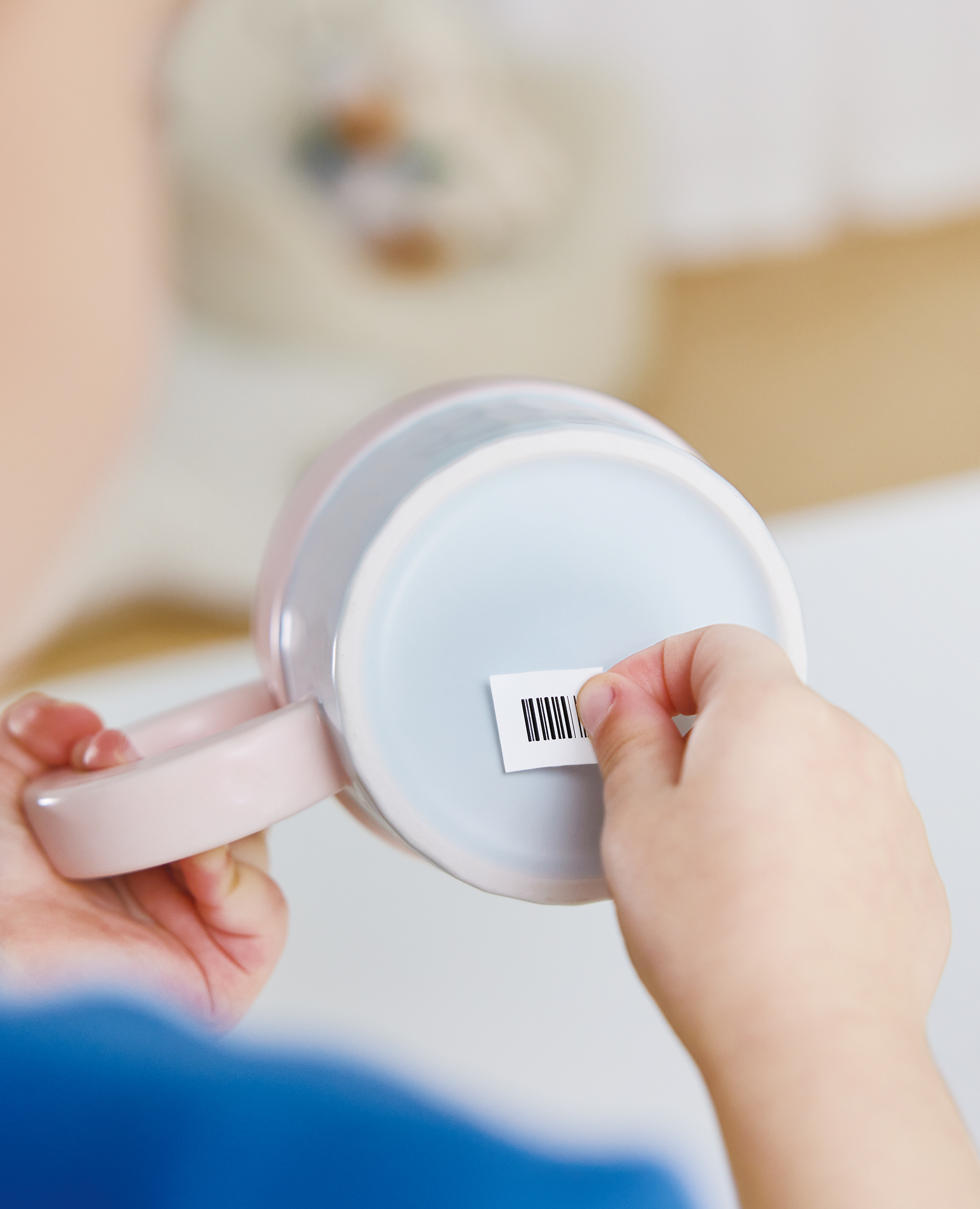 Person applying barcode sticker to the bottom of a pink mug in a home setting.